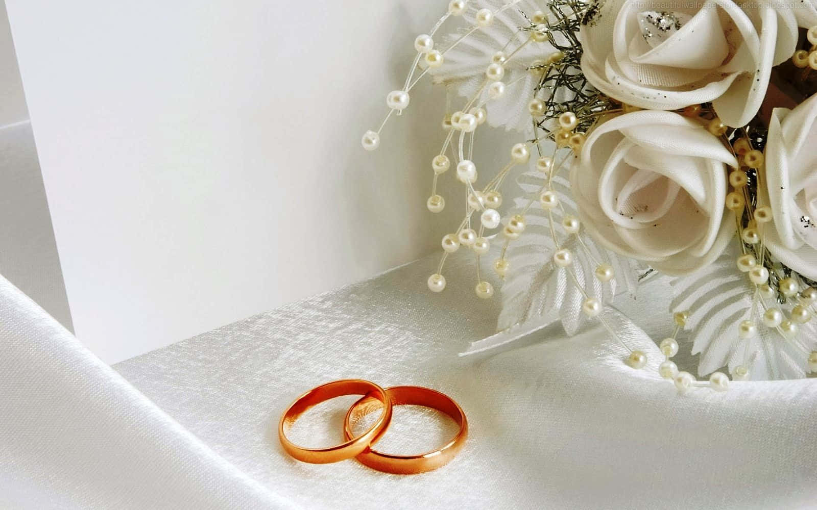 兩個金色結婚戒指旁邊有一束帶珍珠的白色花束。