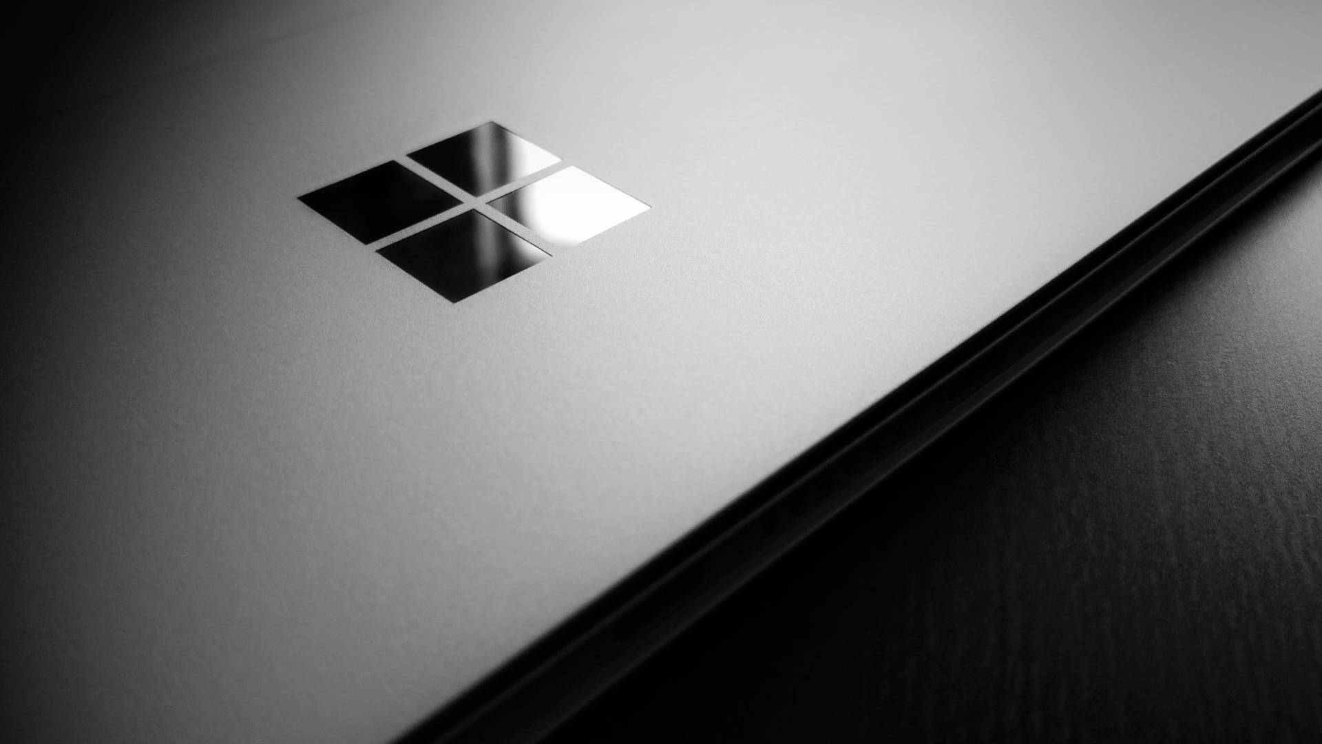 microsoft 桌布 壁紙 — 柔和的攝影棚燈光下，帶有反光Microsoft標誌的時尚銀色筆記本電腦蓋的特寫。