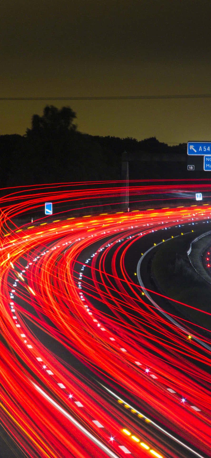夜間高速公路，紅色汽車燈光在黑暗中蜿蜒形成條紋。