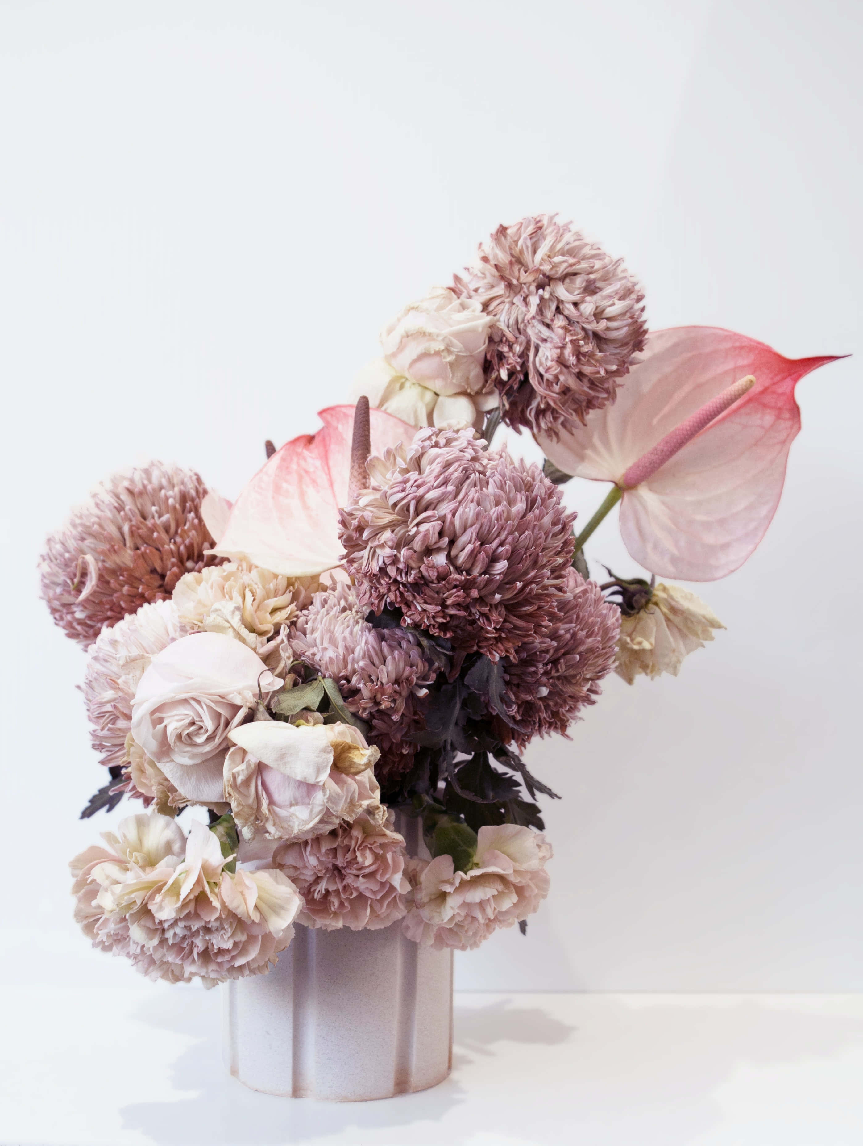 Floral Arrangement 桌布 壁紙 — 柔和粉彩花卉佈置，包括玫瑰、菊花和紅掌，置於有紋理的花瓶中，以簡約白色背景襯托。