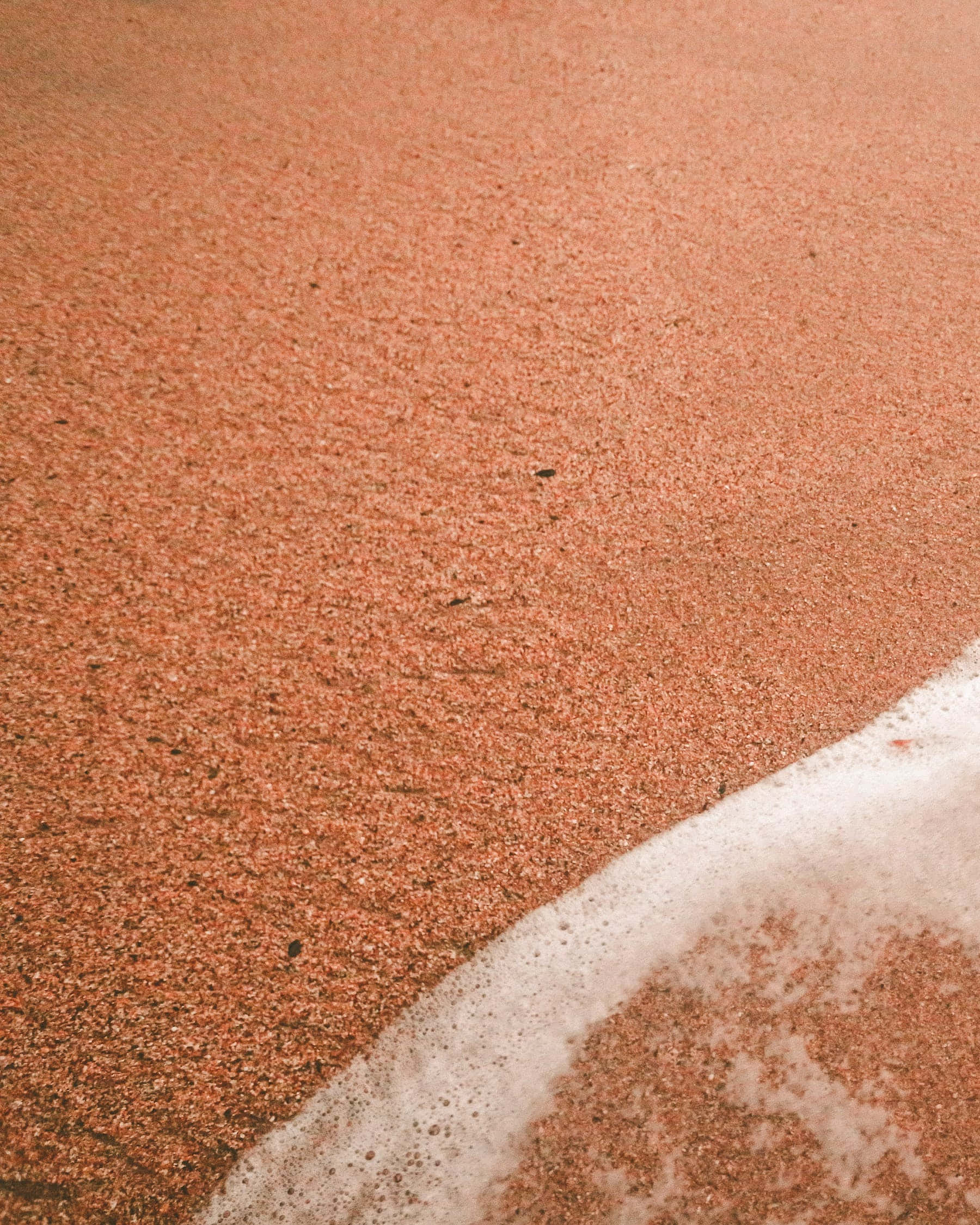 Beach Sand 桌布 壁紙 — 柔和自然光下，細膩的紅褐色沙灘上輕柔的海浪泡沫的特寫。