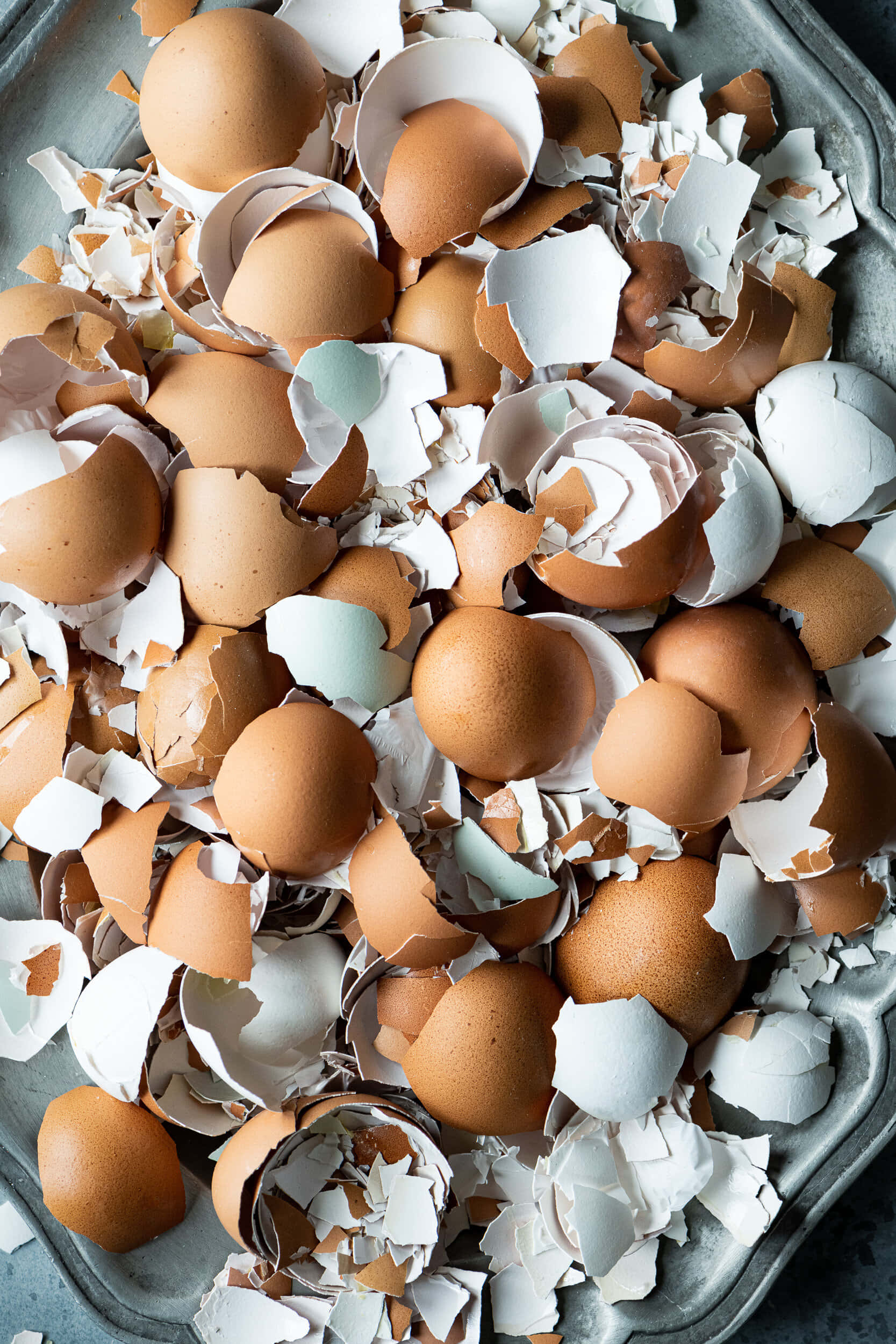 Eggshell 桌布 壁紙 — 柔和自然光下，金屬托盤中散落的破碎棕色和白色蛋殼的特寫。