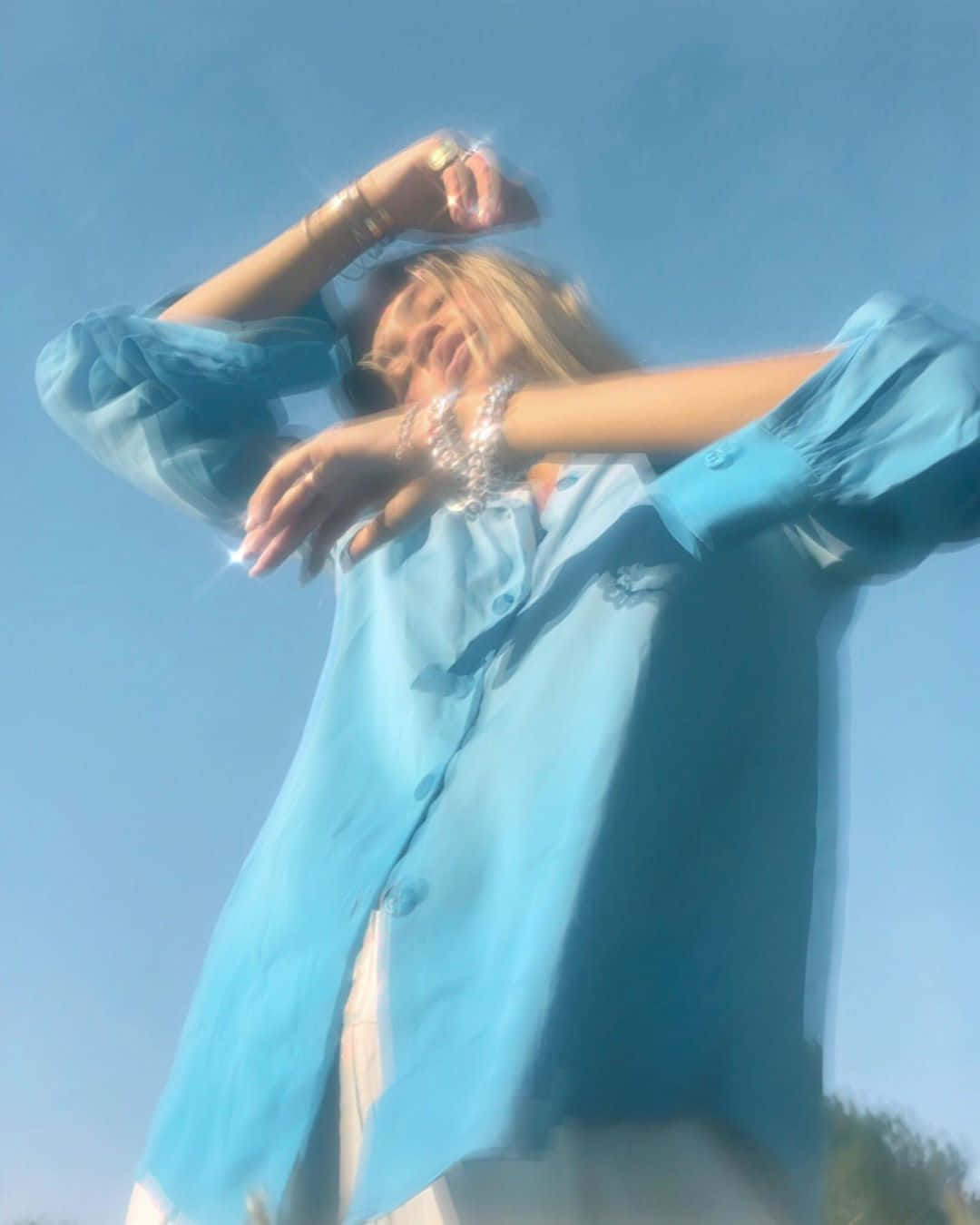 身穿藍色襯衫的女性在明亮的陽光下張開雙臂。