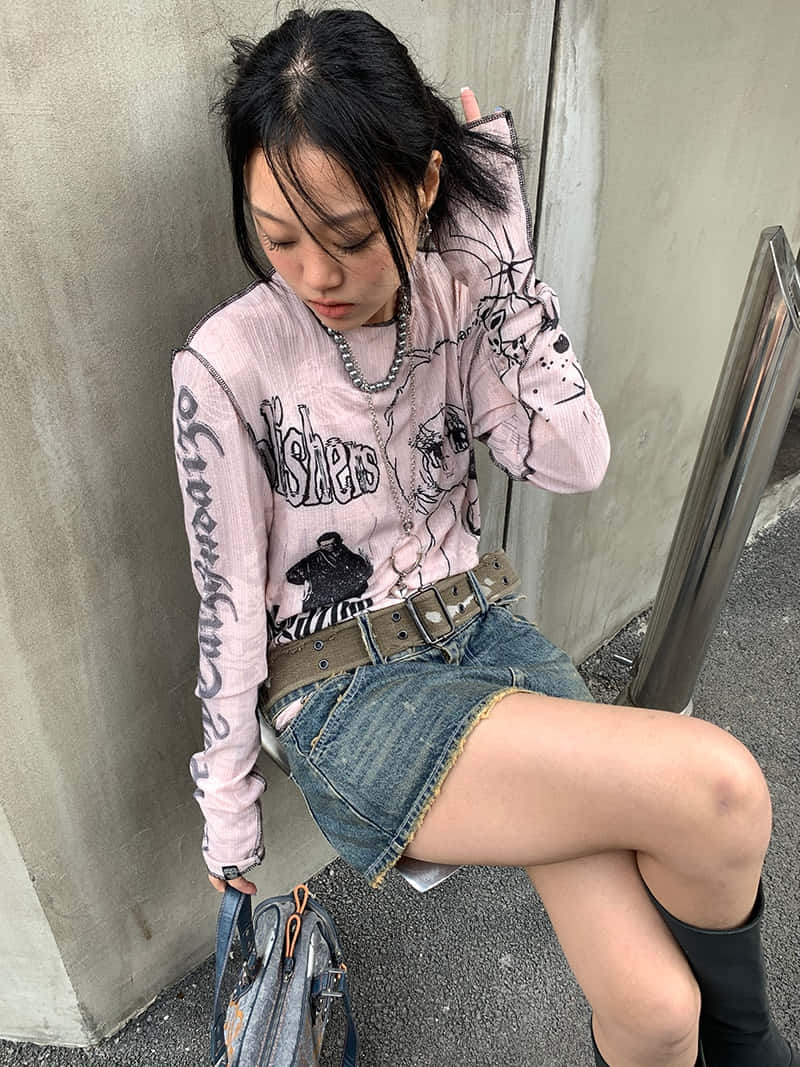 年輕女性穿著粉紅色毛衣和牛仔短褲靠著混凝土牆。
