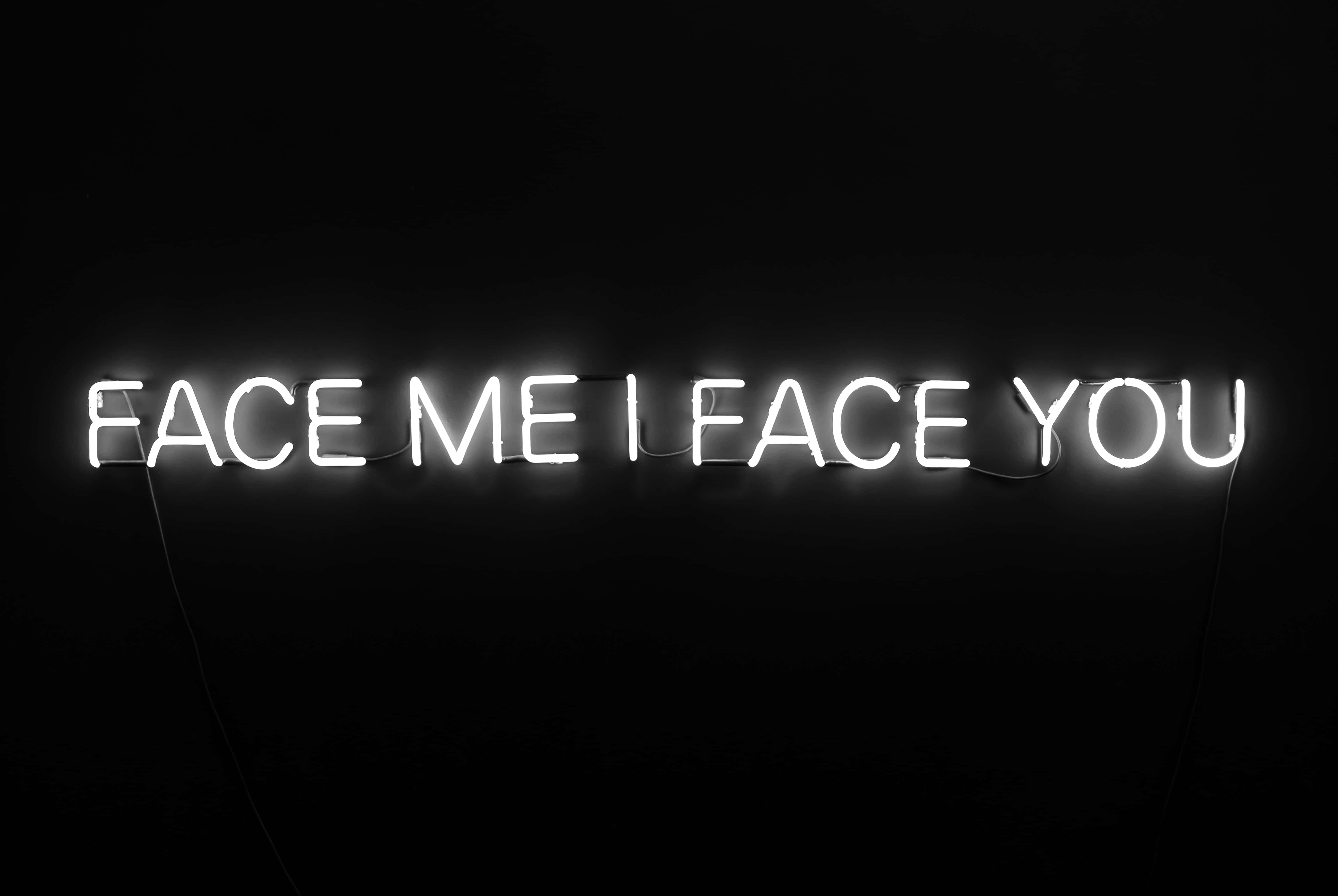 柔軟清潔的白色背景 壁紙 — 一個發光的白色霓虹燈牌寫著 face me i face you，背景是漆黑牆壁。