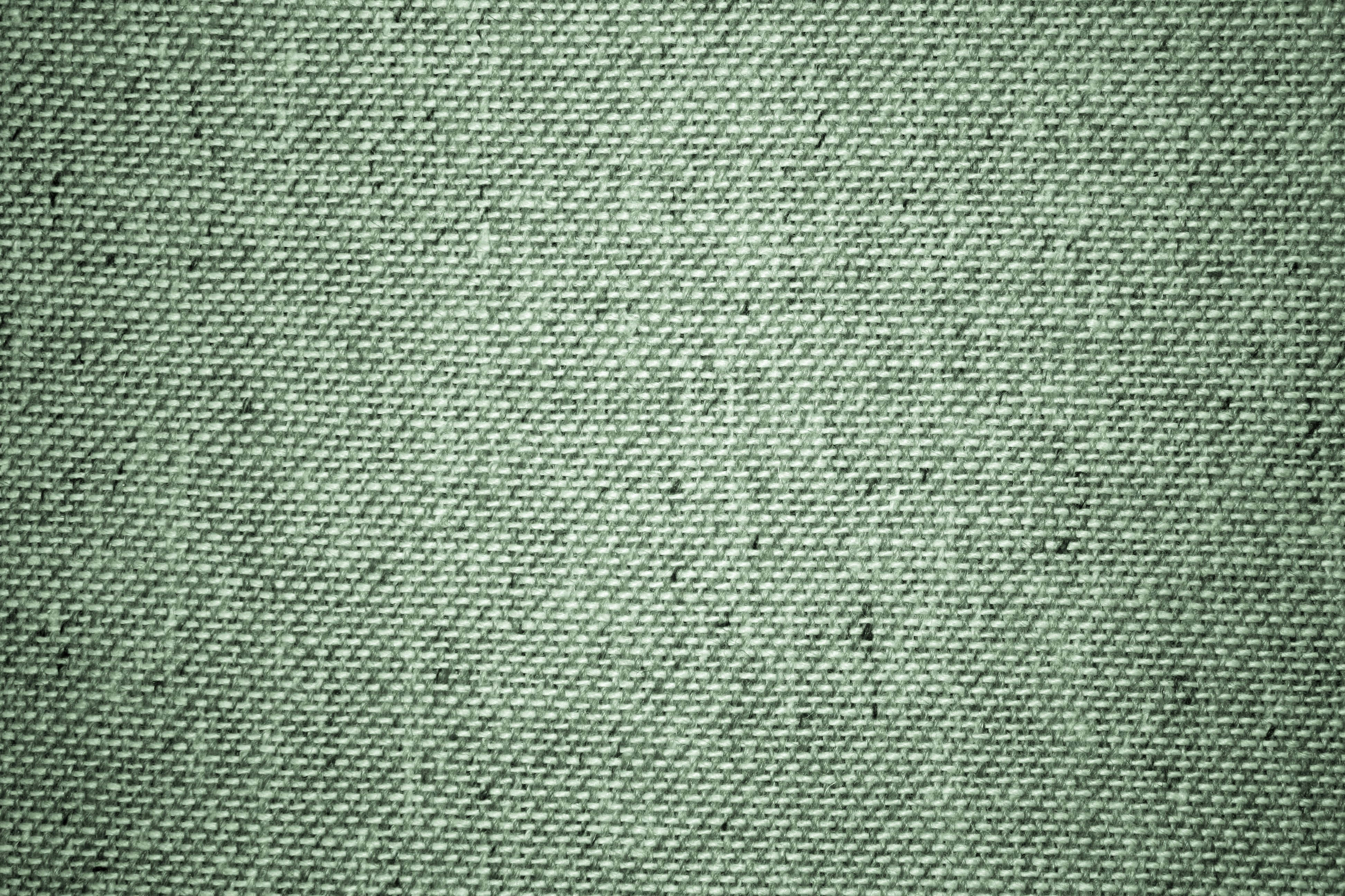sage green aesthetic 桌布 壁紙 — 柔軟燈光下，帶有可見織紋和細微斑點的綠色紋理布料特寫。