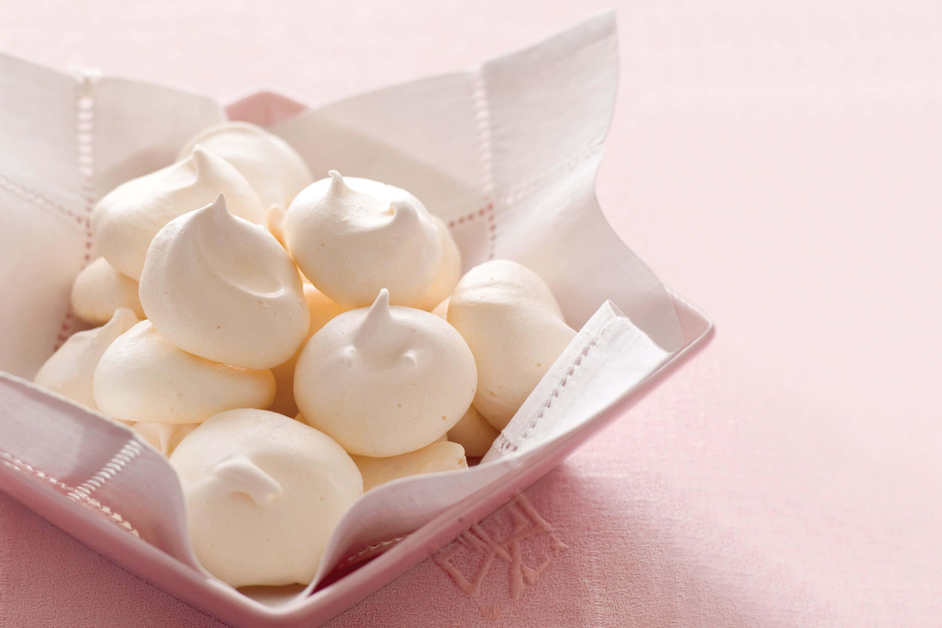 Meringue 桌布 壁紙 — 柔軟的白色蛋白霜之吻放在鋪有精緻紙張的粉紅色碗中，置於粉彩粉紅布上。