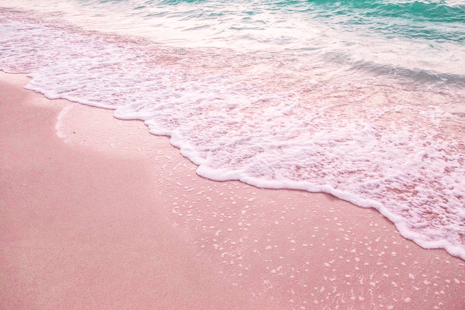 Beach Desktop 桌布 壁紙 — 柔軟的粉紅色沙灘遇上碧綠色的海浪，形成一個寧靜的海岸場景，帶有輕柔的泡沫。