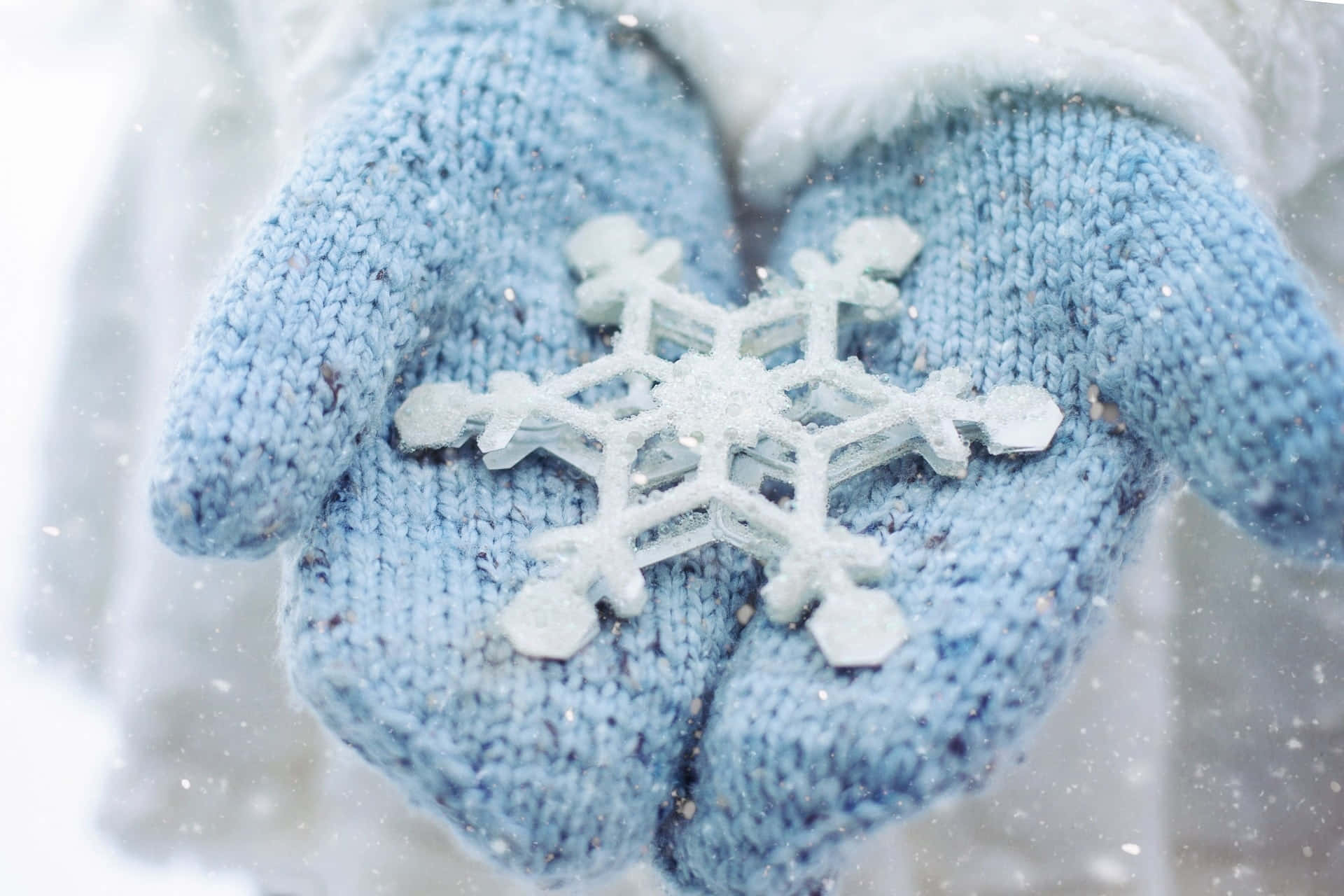 Mittens 桌布 壁紙 — 柔軟的藍色針織手套在雪景背景下輕托著精緻的雪花。