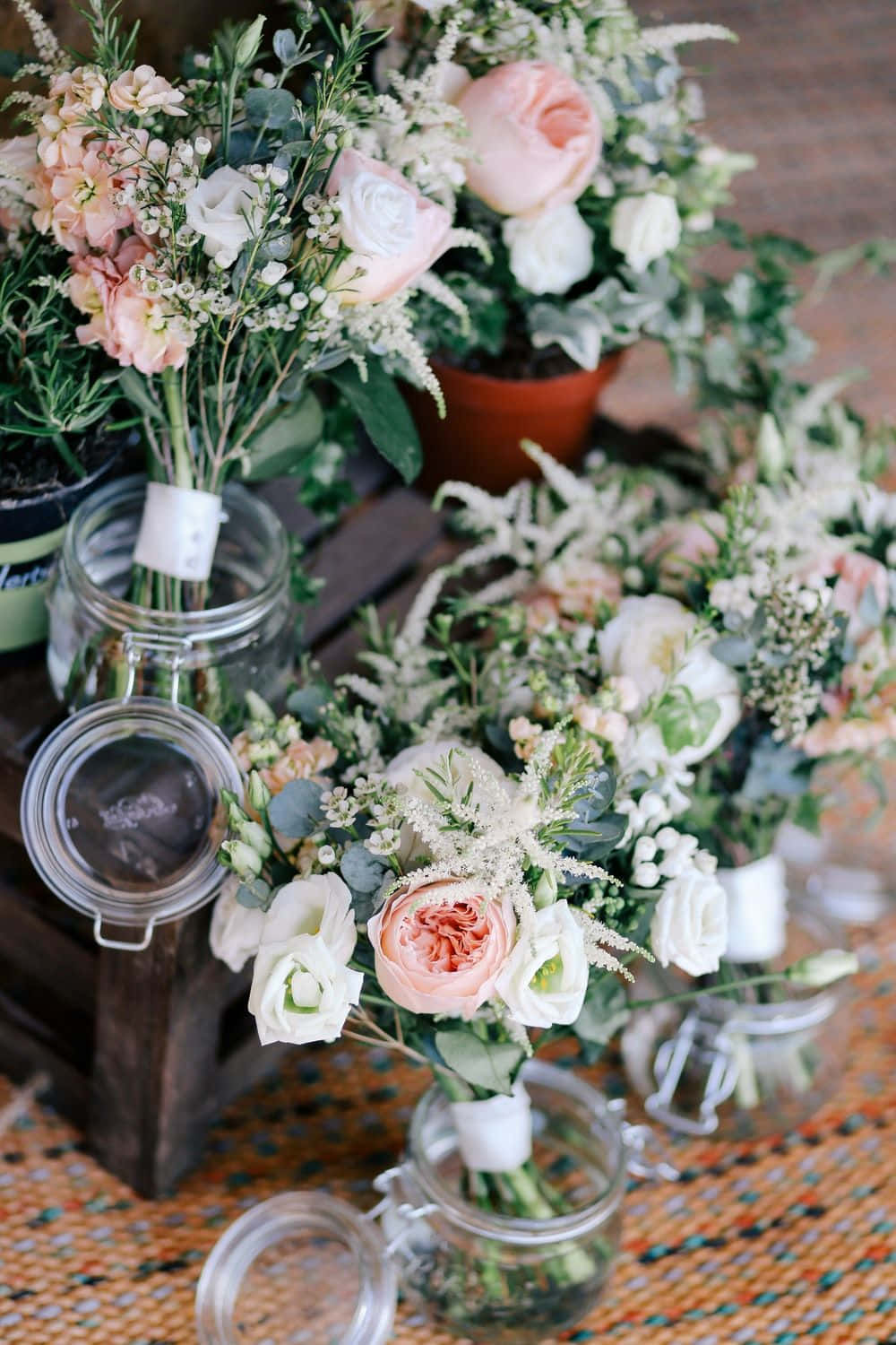 Wedding Flowers 桌布 壁紙 — 柔軟的蜜桃色和白色玫瑰配綠葉，擺放在玻璃罐中置於編織墊上。