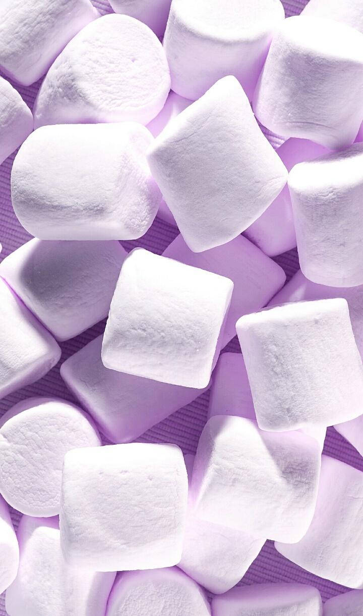 Marshmallow 桌布 壁紙 — 柔軟紫色紋理表面上散落著 fluffy 白色棉花糖的特寫。