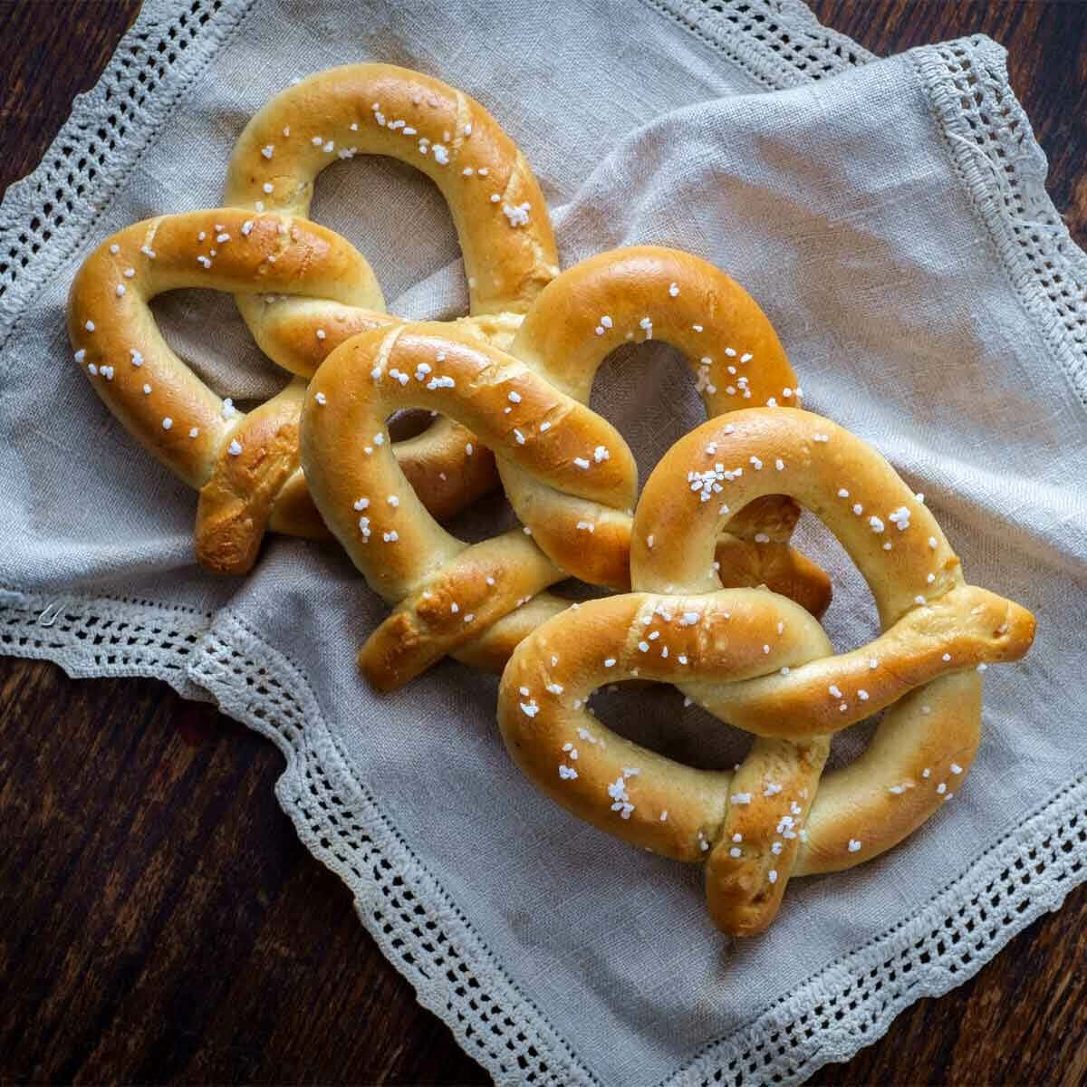 柔軟美味——椒鹽卷餅的完美之選！ 壁紙 — 金黃色的蝴蝶餅撒上粗鹽，誘人地放在深色木桌上帶蕾絲邊的布上。