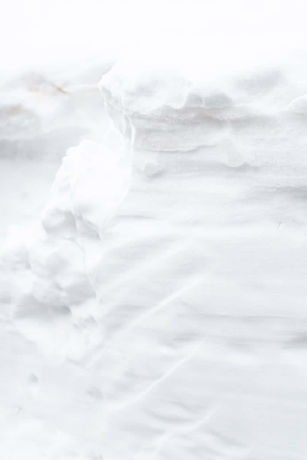 白色 iPhone 桌布 壁紙 — 柔軟質感的白色雪堆，帶有微妙的灰色和米色底色，營造出寧靜的冬日景觀。