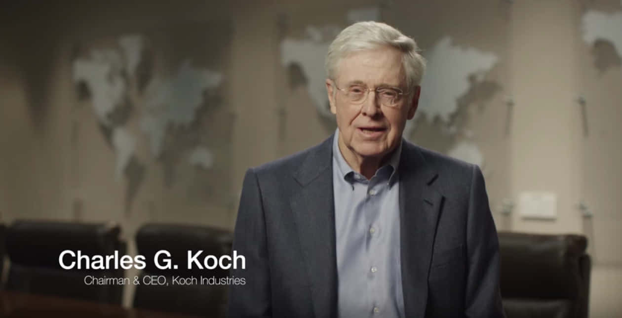 Charles G Koch 身穿西裝，站在辦公室裡，背景是世界地圖。
