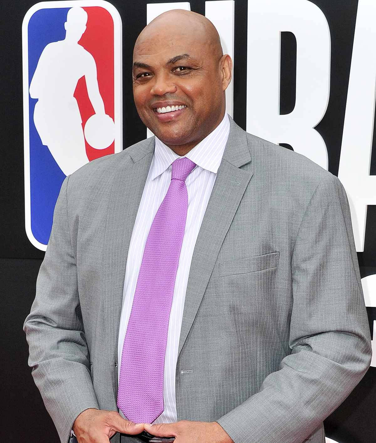 一位身穿灰色西裝和紫色領帶的男士在NBA活動中微笑。