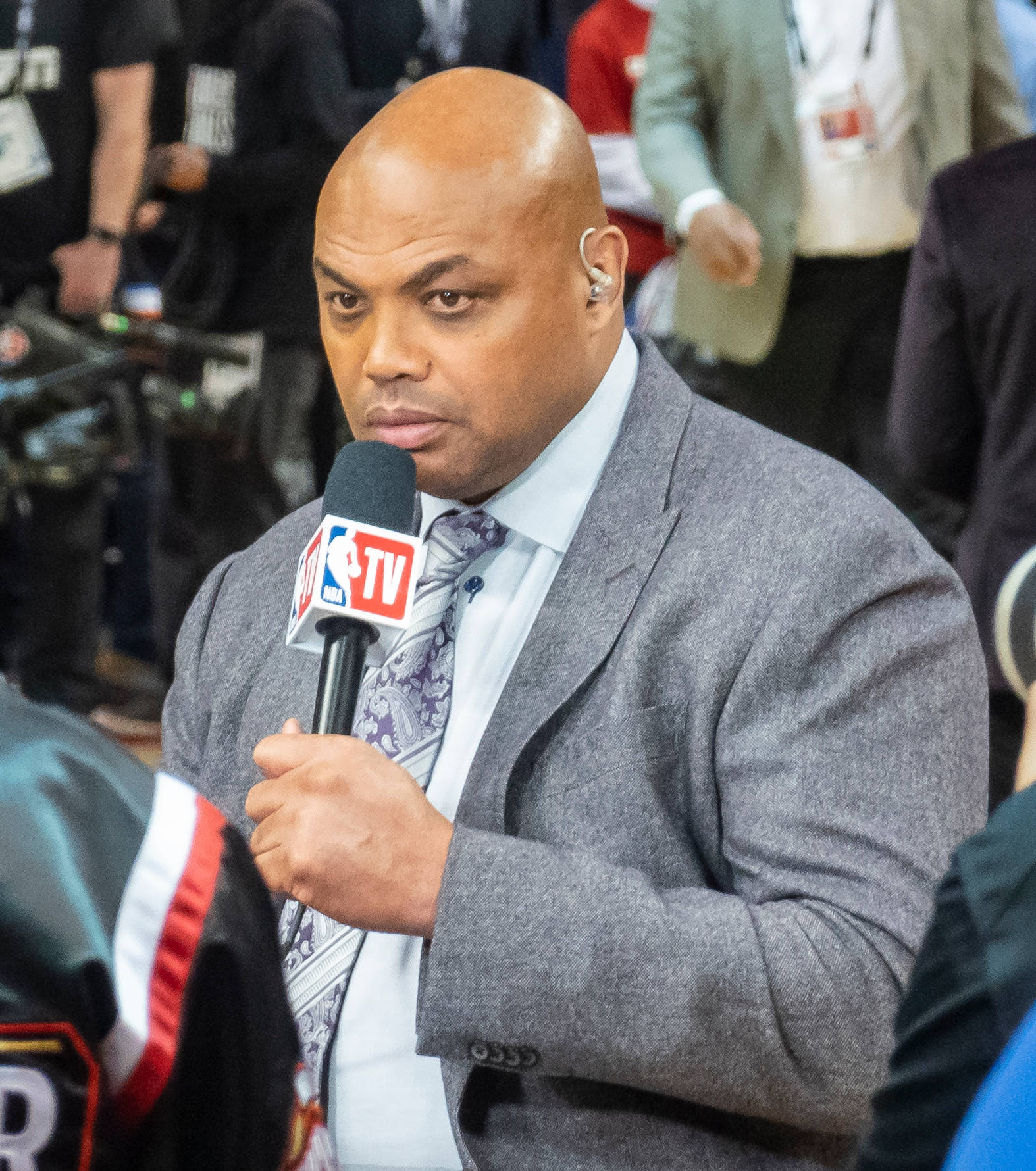 NBA TV體育記者穿著灰色西裝，在直播中手持麥克風。
