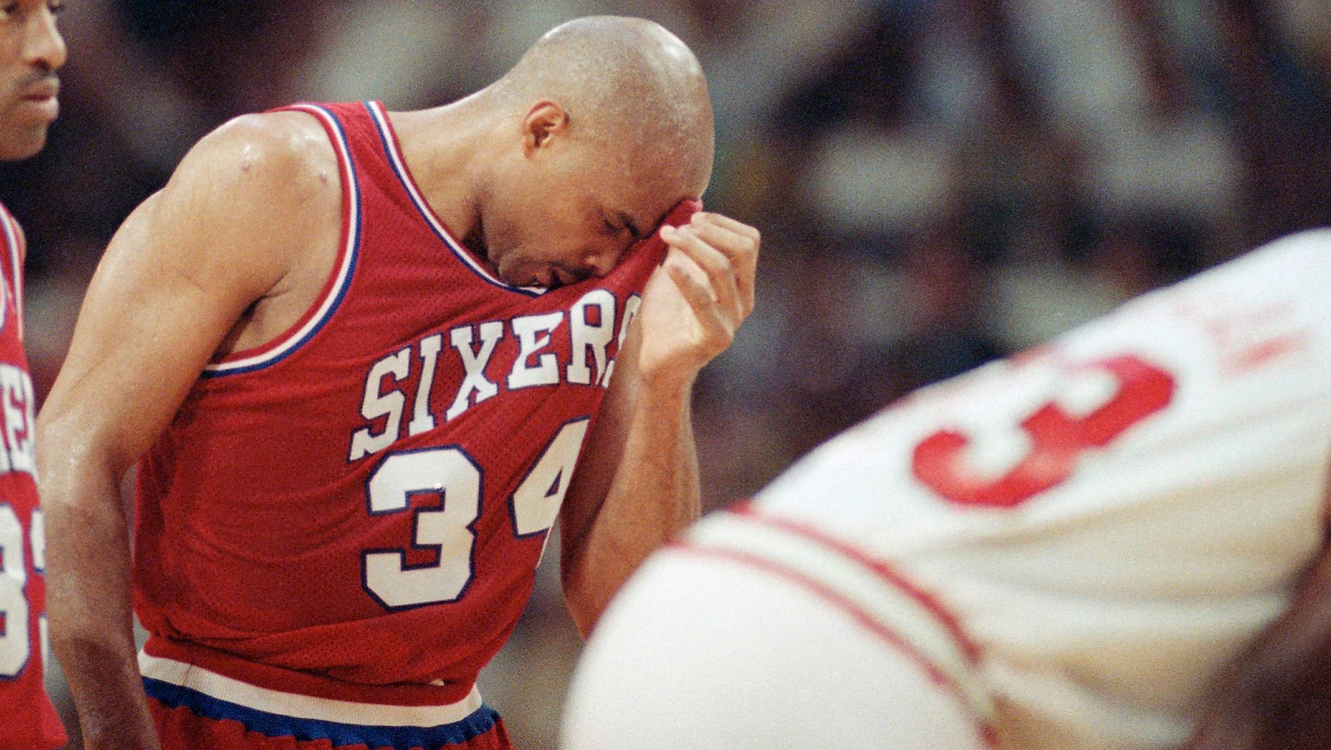查理斯·巴克利七六人隊比賽 壁紙 — 一名身穿紅色Sixers球衣、背號34的籃球運動員在賽後用球衣擦臉。