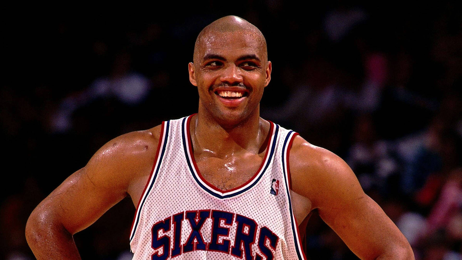 身穿Sixers球衣的籃球運動員微笑雙手叉腰。