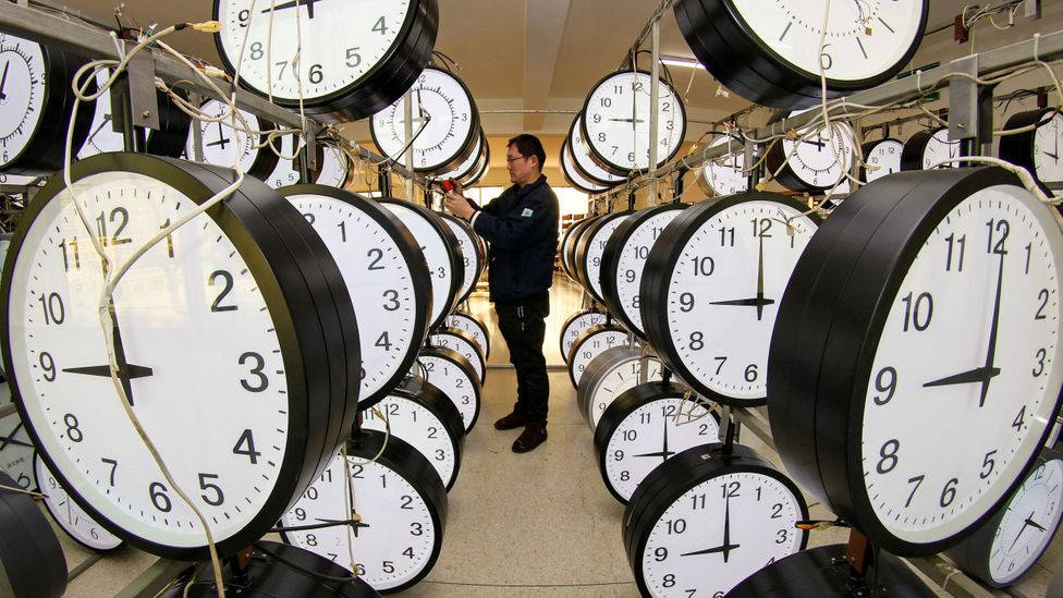 技術人員在一個掛滿指針時鐘的工廠裡調整時鐘。