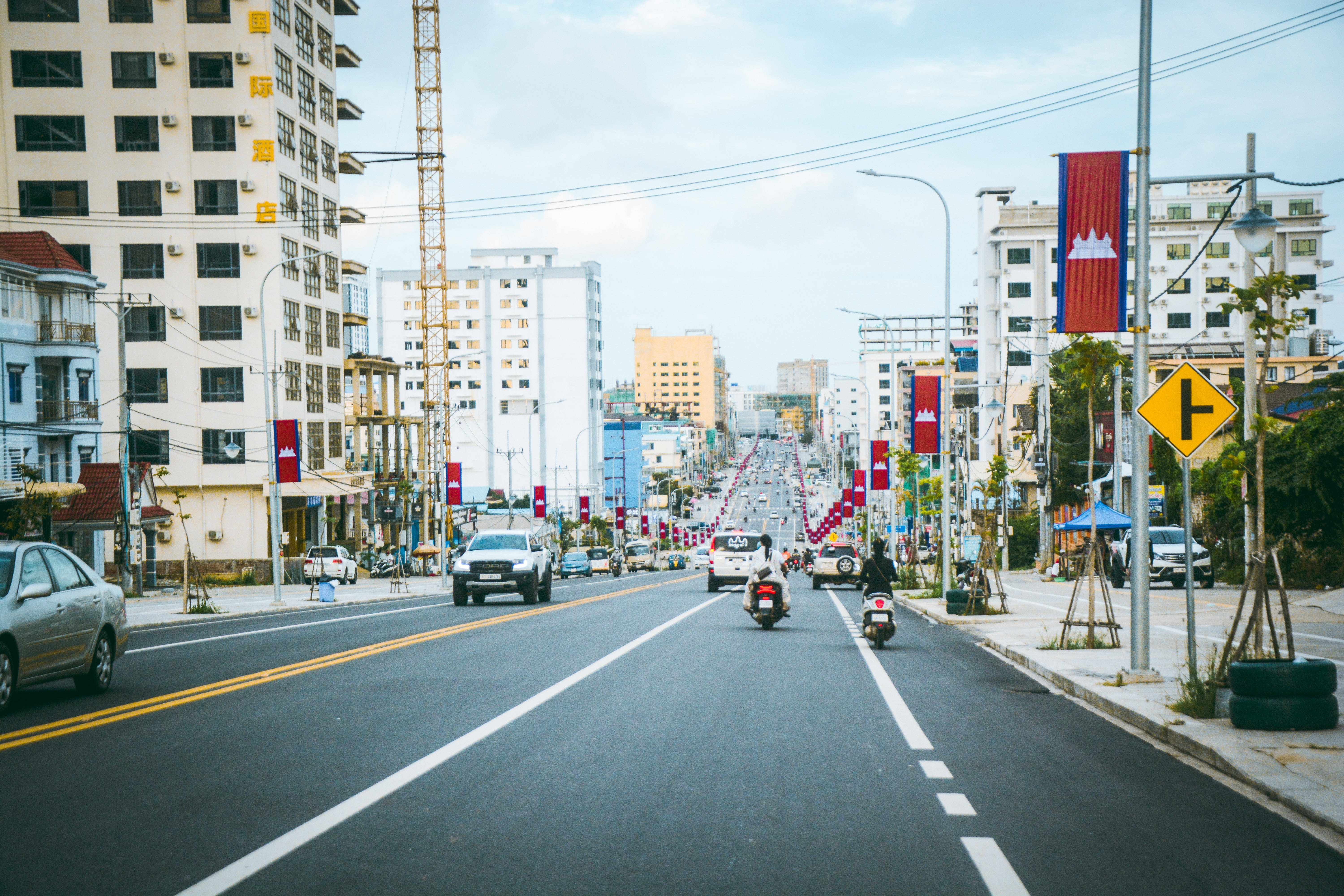 柬埔寨城市高速公路 壁紙 — 柬埔寨一條寬闊的城市街道，兩旁建築物和紅色國旗在明亮的白天天空下。