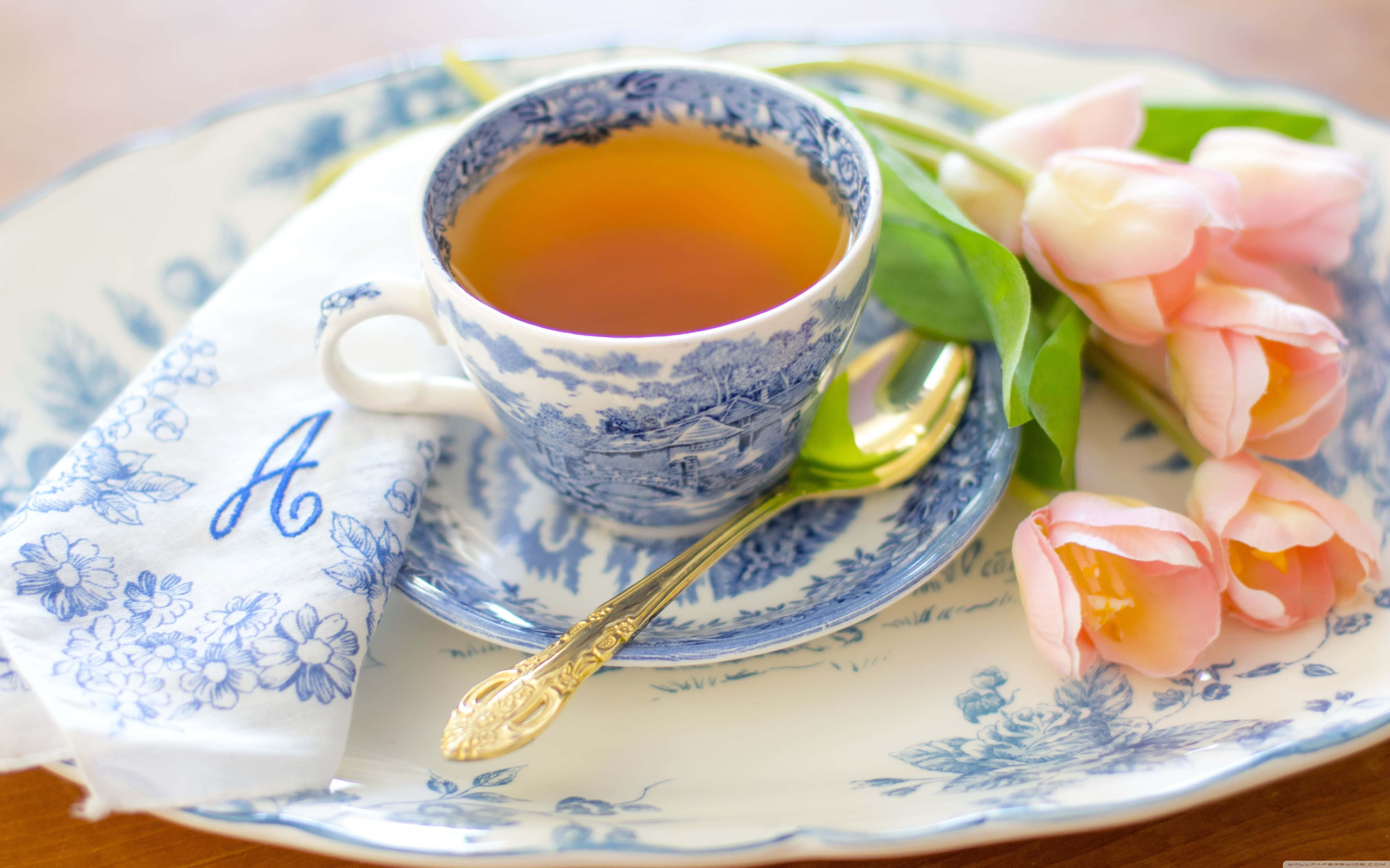 柳枝茶具茶杯圖 壁紙 — 一個精緻的青花瓷茶杯盛滿琥珀色茶，放在配套的茶碟上，旁邊有柔和的粉紅色鬱金香和一把金匙。