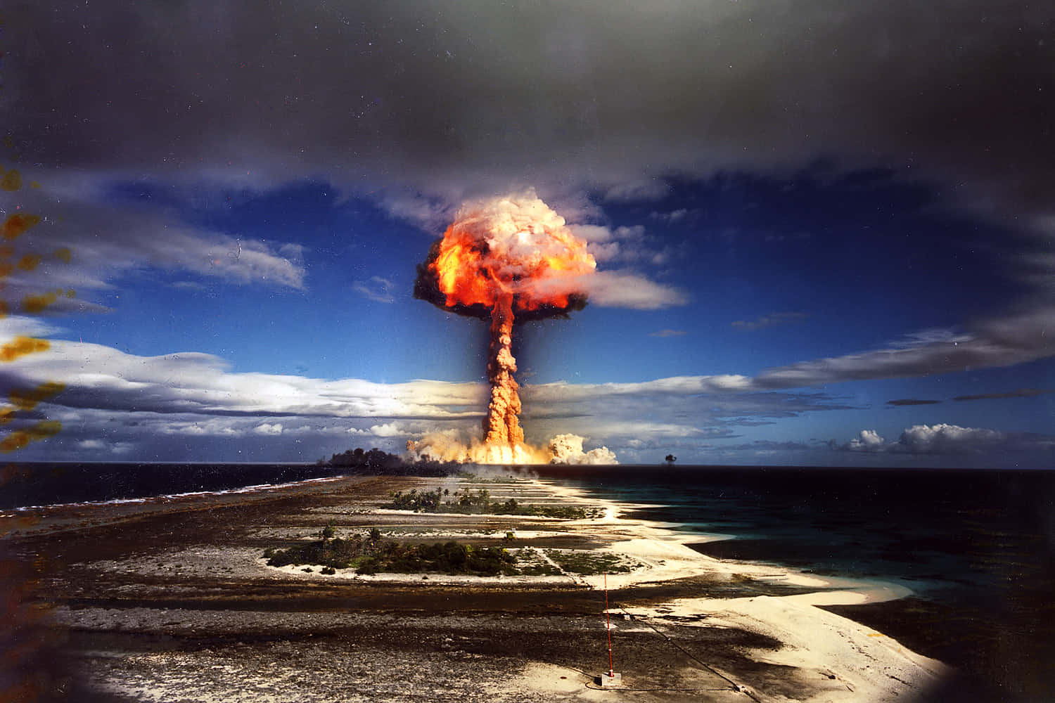 Fallout Nuke 桌布 壁紙 — 核爆炸在熱帶環礁上空爆發，在戲劇性的藍天下投射出橙色蘑菇雲。