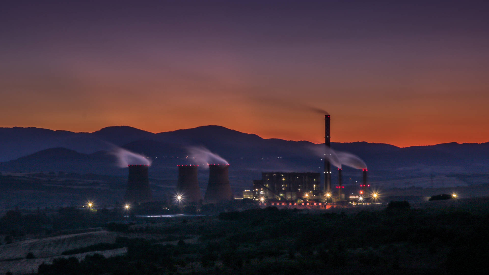 黃昏時的工業發電廠，蒸汽在橙色天空和山巒襯托下升起