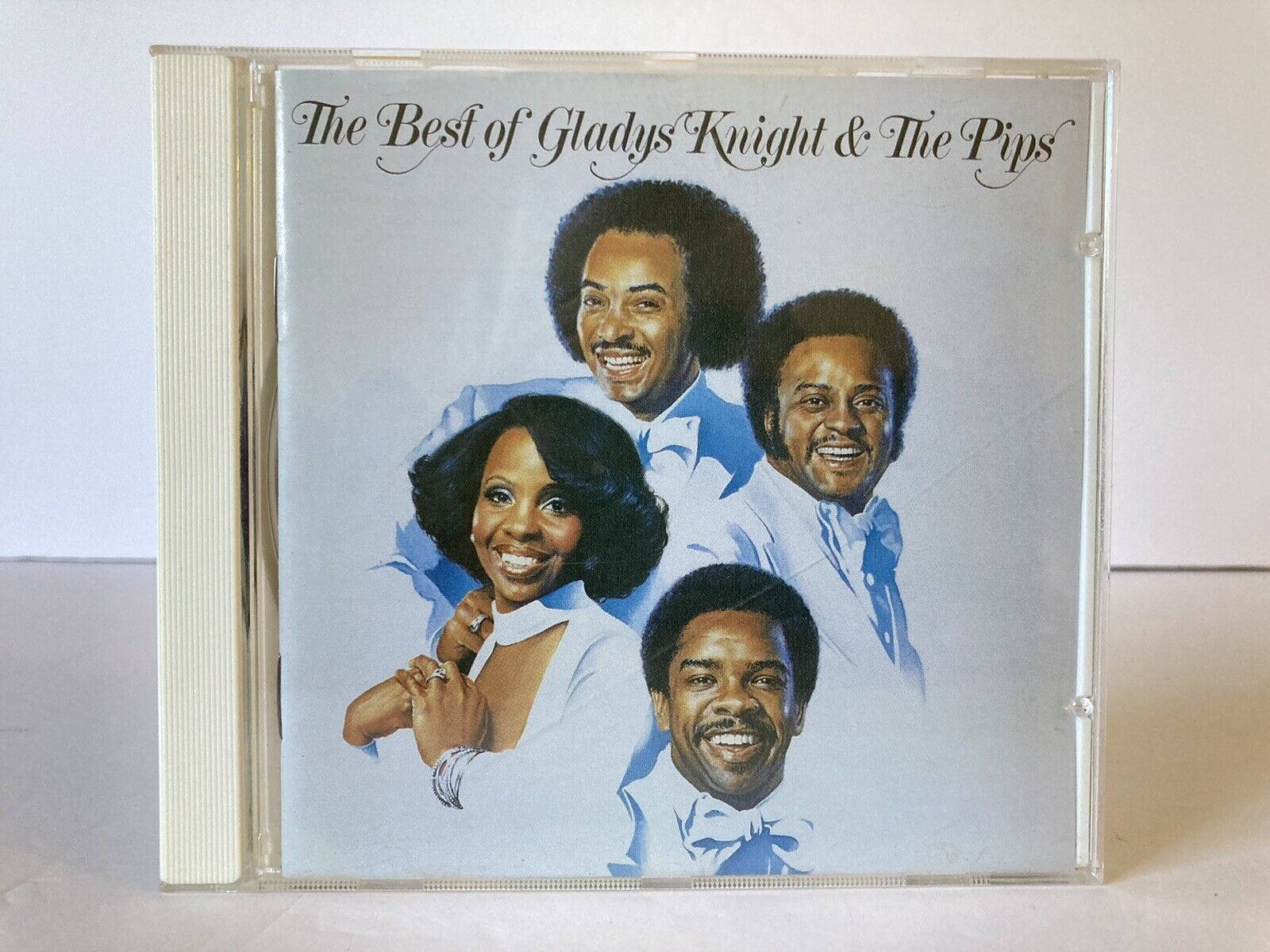 格拉迪斯·奈特與合唱團經典專輯 壁紙 — 一張復古CD封面，Gladys Knight and The Pips 穿著淺藍色西裝，在柔和的灰色背景前微笑。
