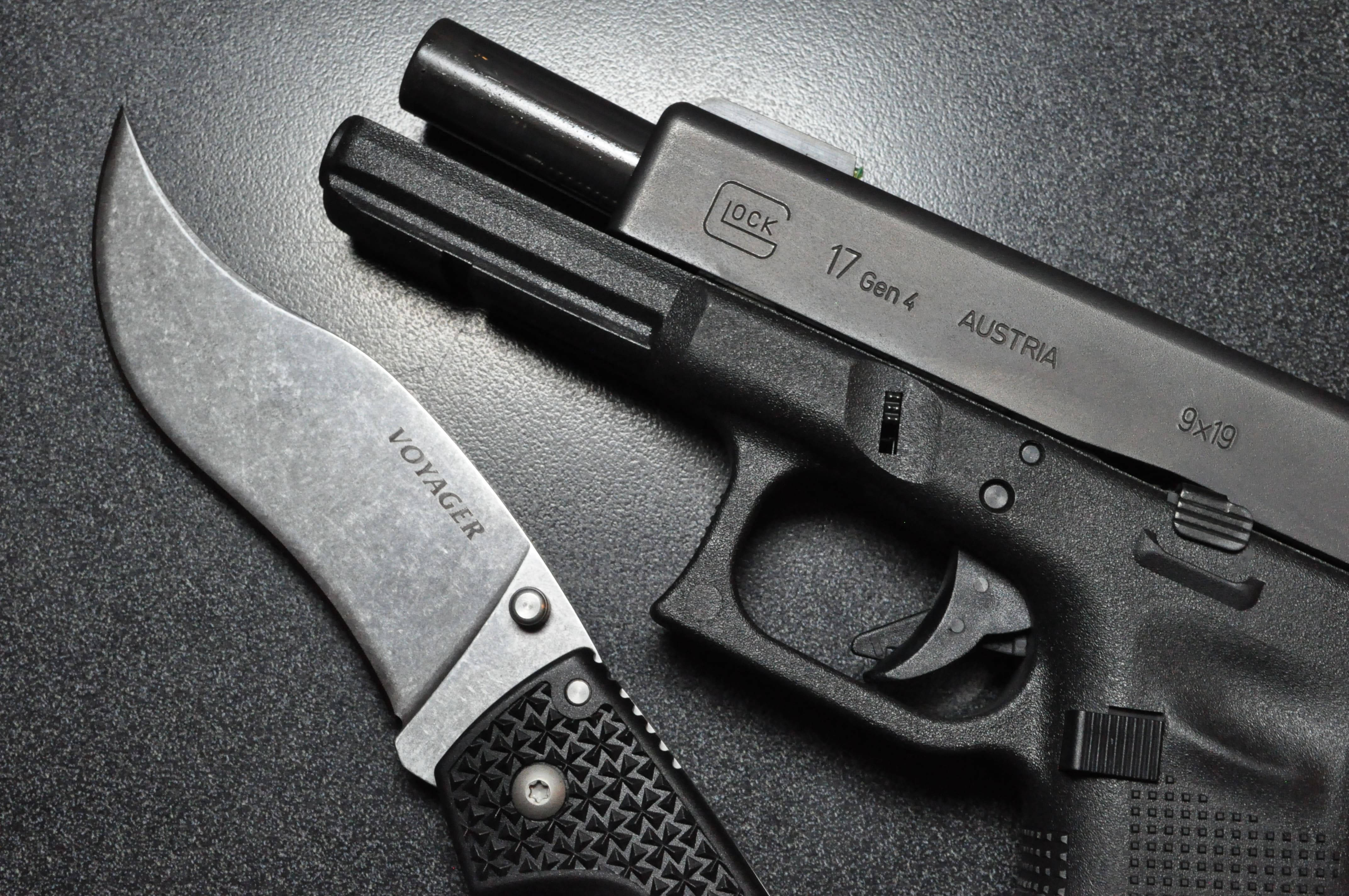 格洛克17配維加刀：戶外完美組合壁紙 壁紙 — 一支時尚的黑色Glock 17 Gen 4手槍和一把Voyager彎刀放在深色紋理表面上，在戲劇性的燈光下。
