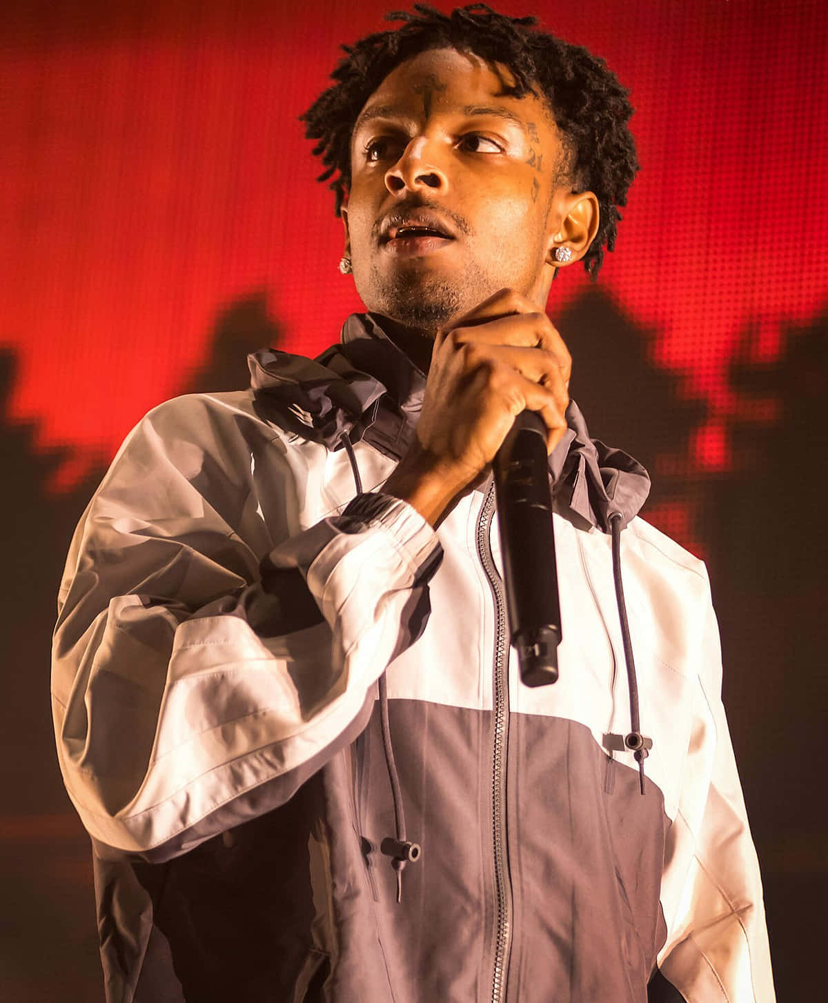 格萊美提名饒舌歌手 21 Savage 舞台熱力演出 壁紙 — 一位留著辮子的男性表演者在強烈的紅色舞台燈光下對著麥克風唱歌。