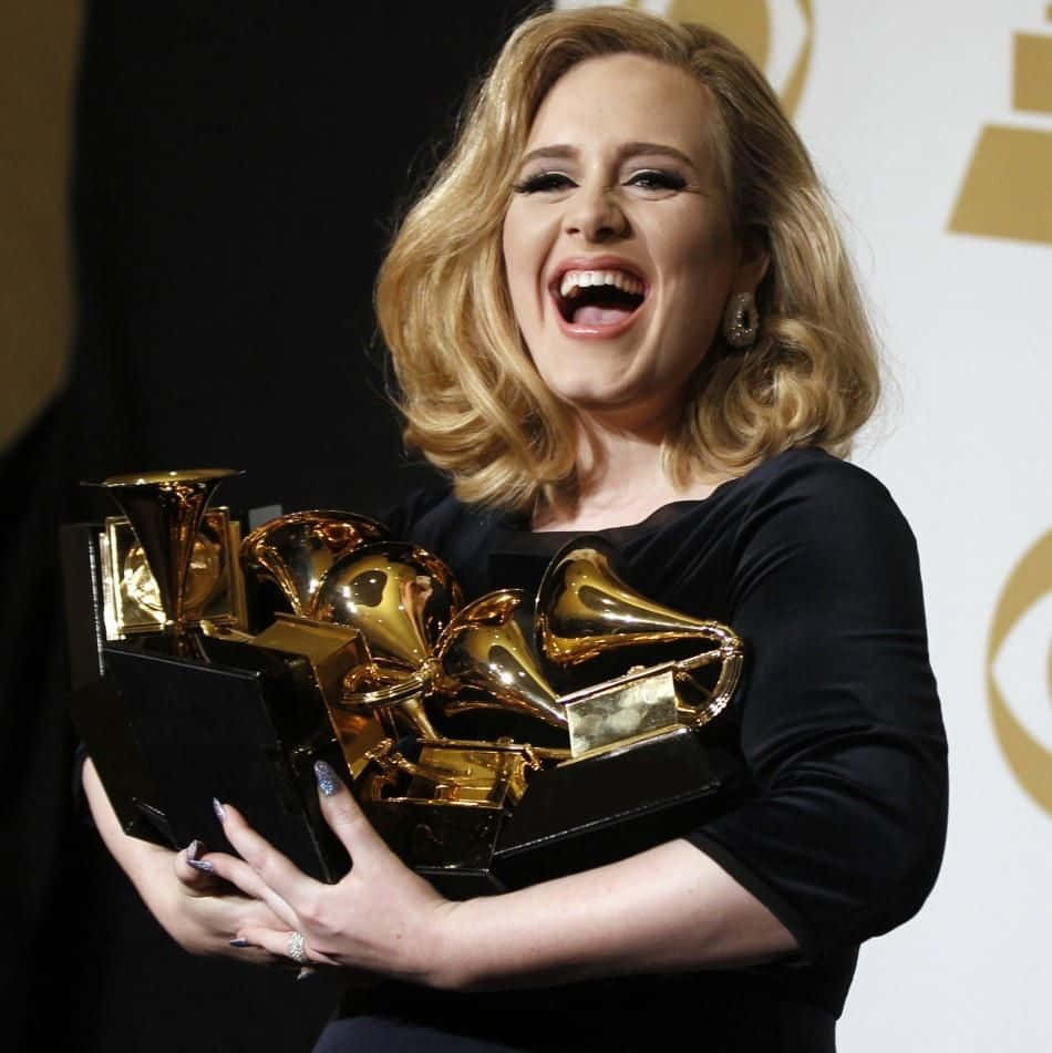 Adele 在舞台上捧著多個格林美獎座大笑。