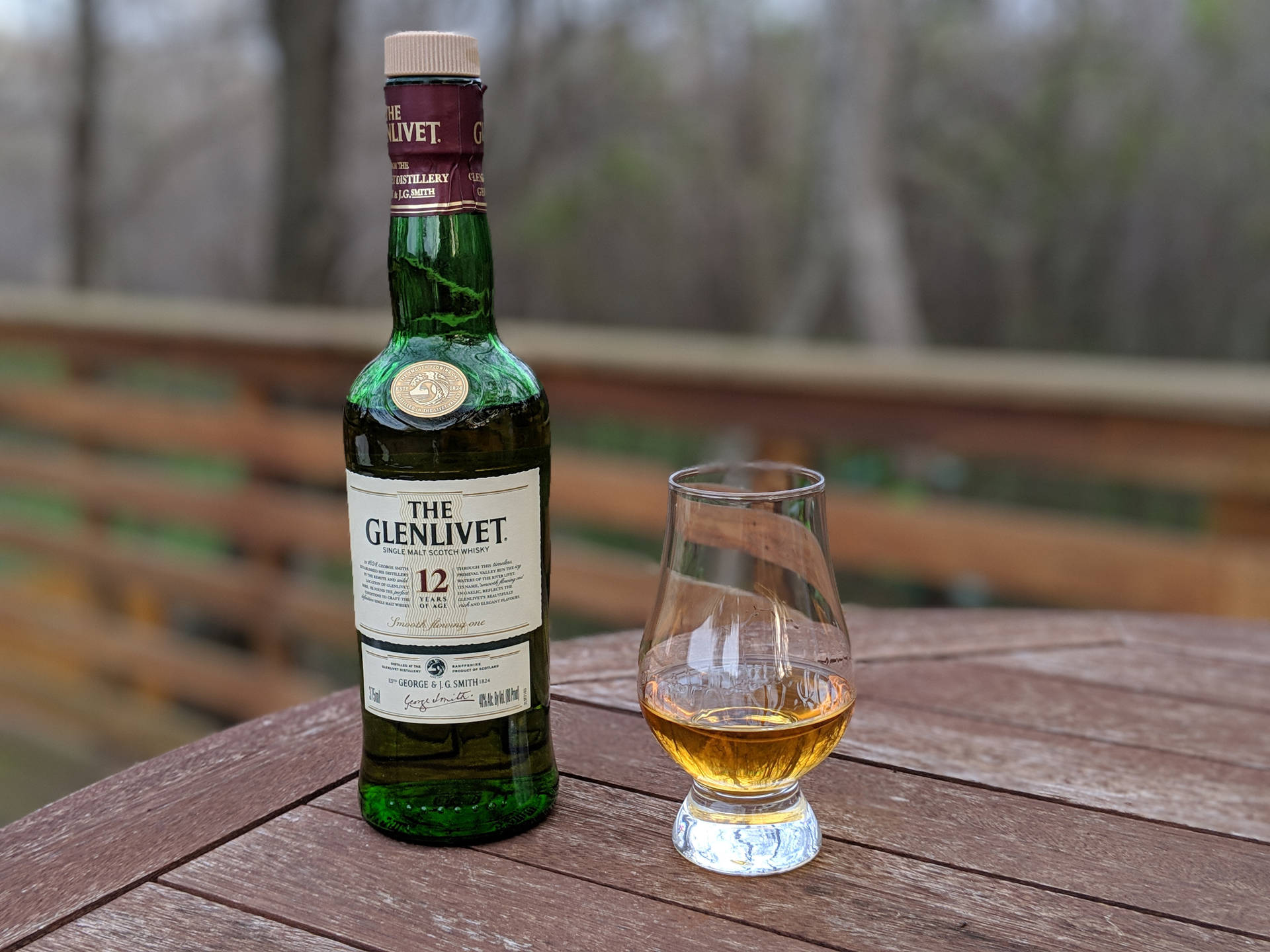 一瓶Glenlivet威士忌和一個品酒杯放在木甲板上。
