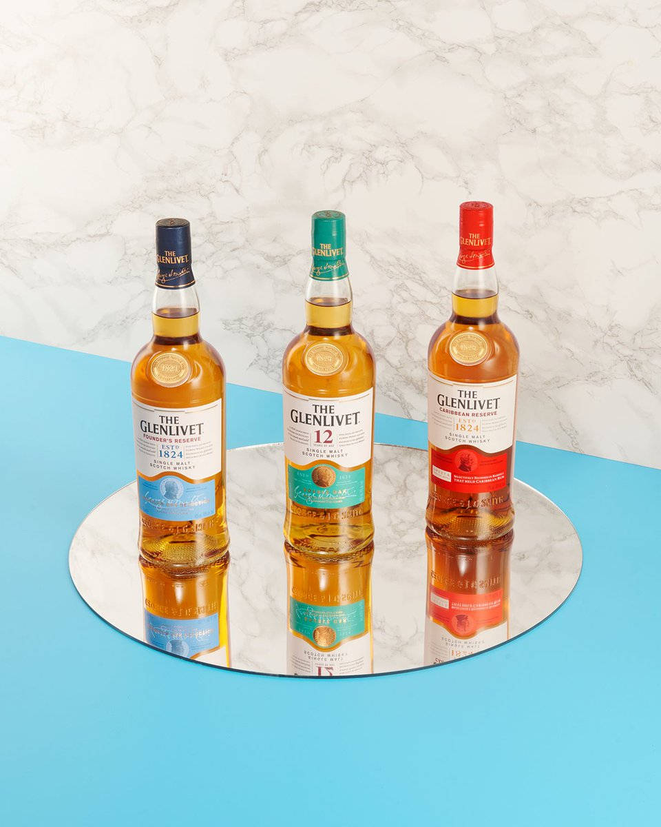 三瓶Glenlivet威士忌酒瓶排列在帶有大理石和藍色背景的鏡面托盤上。