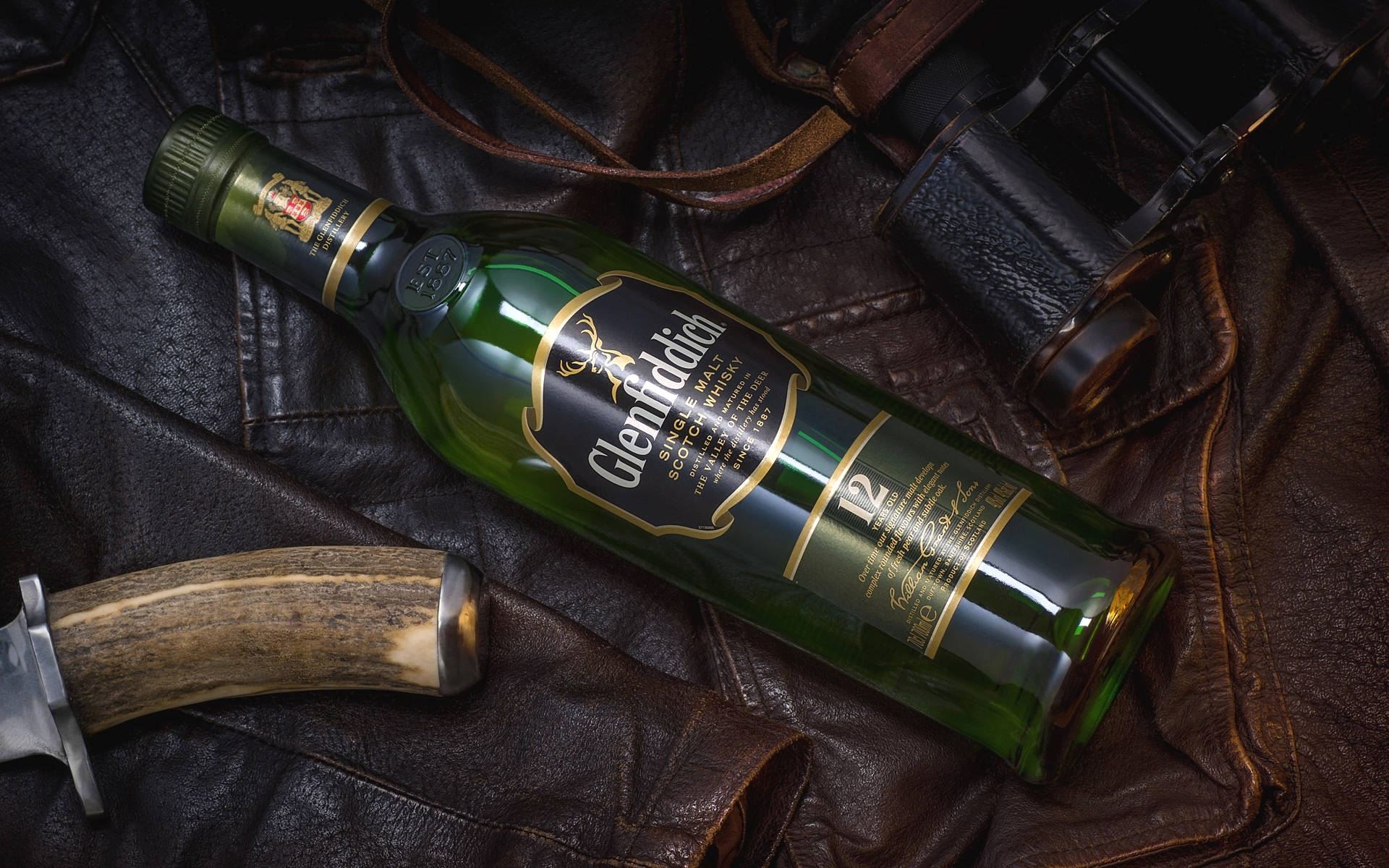 Glenfiddich 威士忌酒樽喺皮革上，附有刀同望遠鏡。