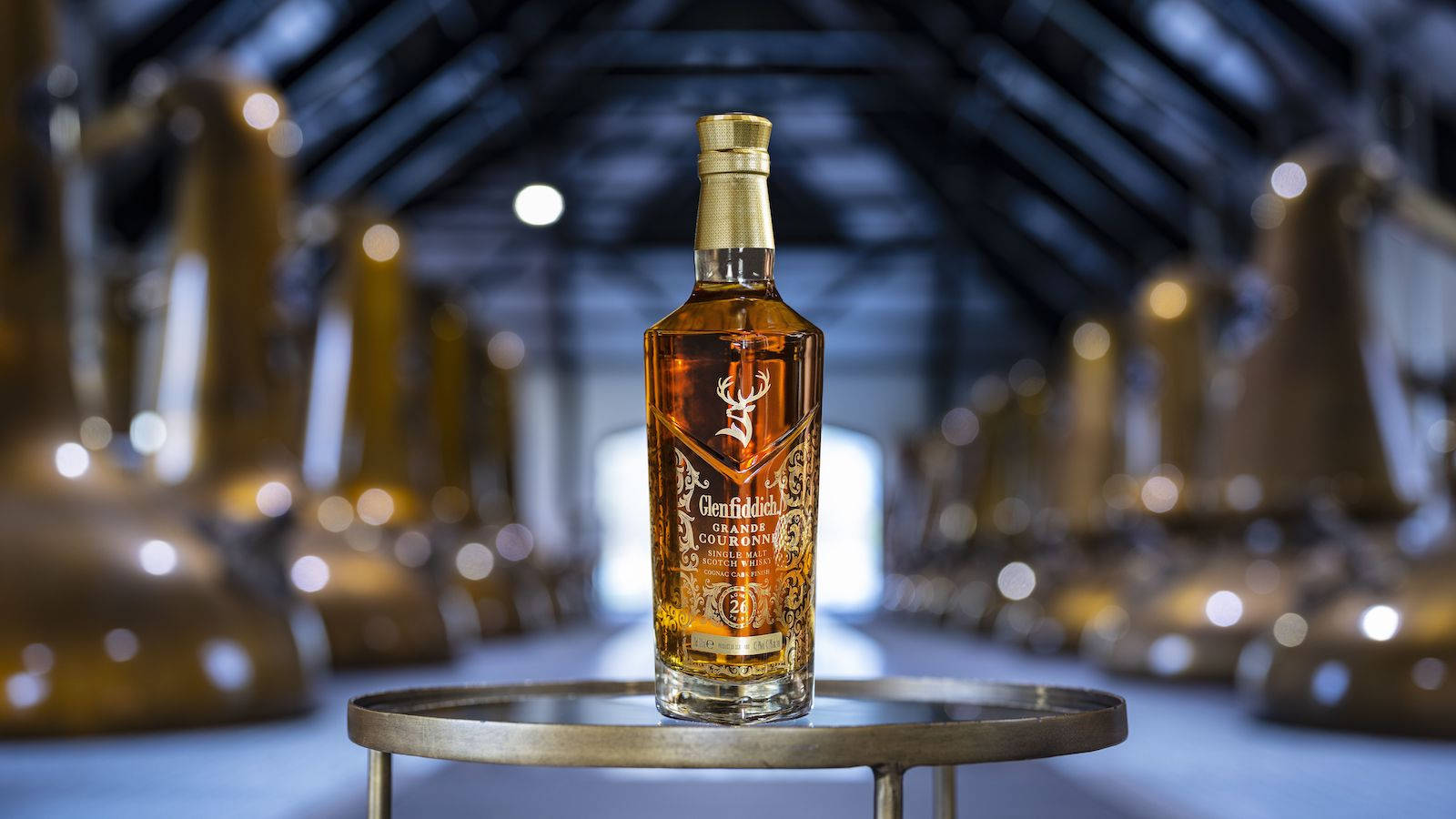 在蒸餾廠中展示的 Glenfiddich 威士忌酒瓶，背景有銅製蒸餾器。