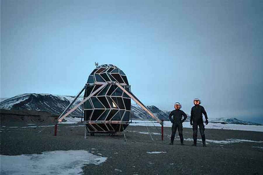 格陵蘭壯麗冰山 壁紙 — 兩名戴著發光頭盔的太空人站在蒼白天空下，雪地外星景觀中的幾何太空棲息地前。