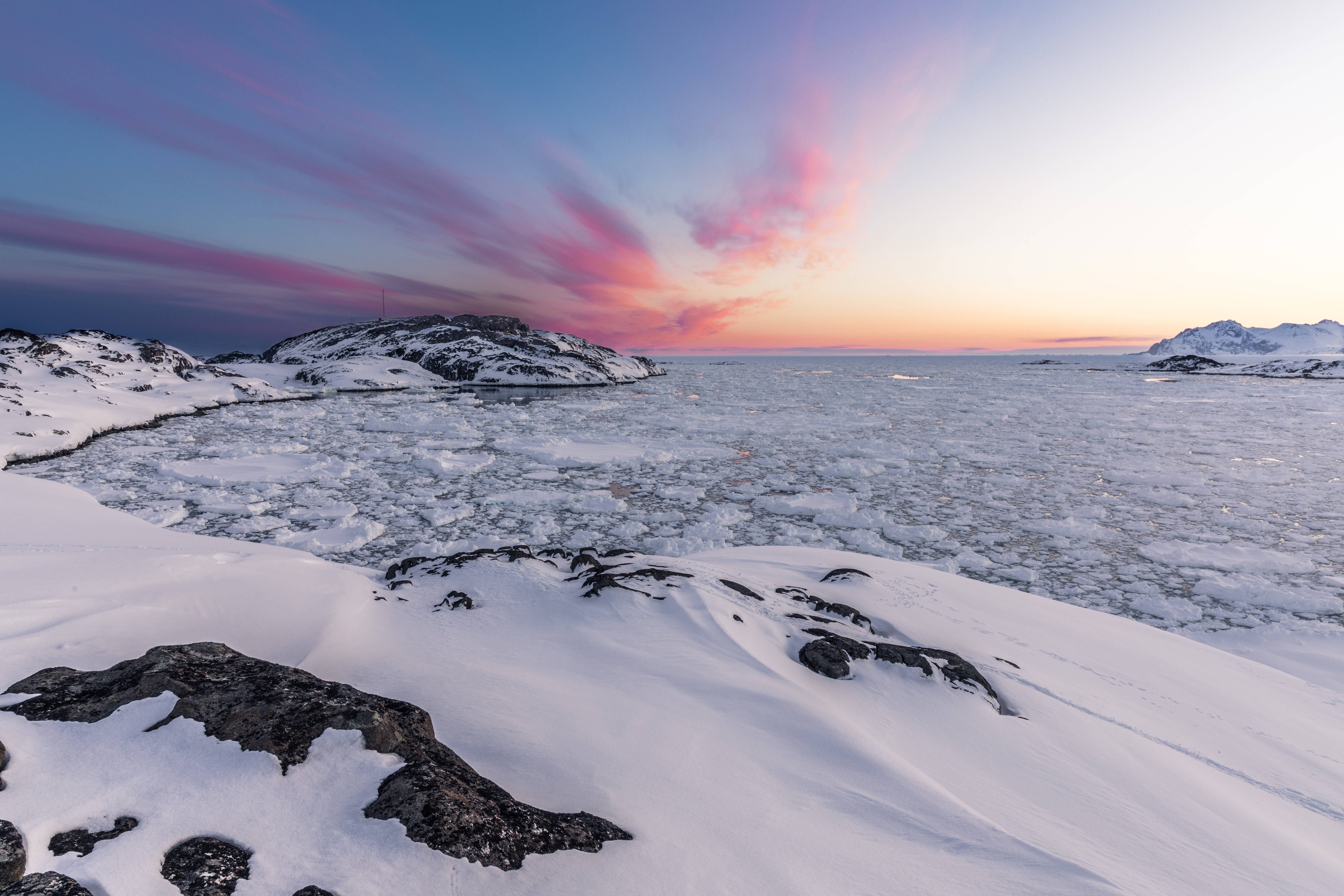 格陵蘭島凍結海面 壁紙 — 日落時分的冰封海岸景觀，雪覆蓋的岩石和浮冰在粉紅色和藍色雲彩的天空下。