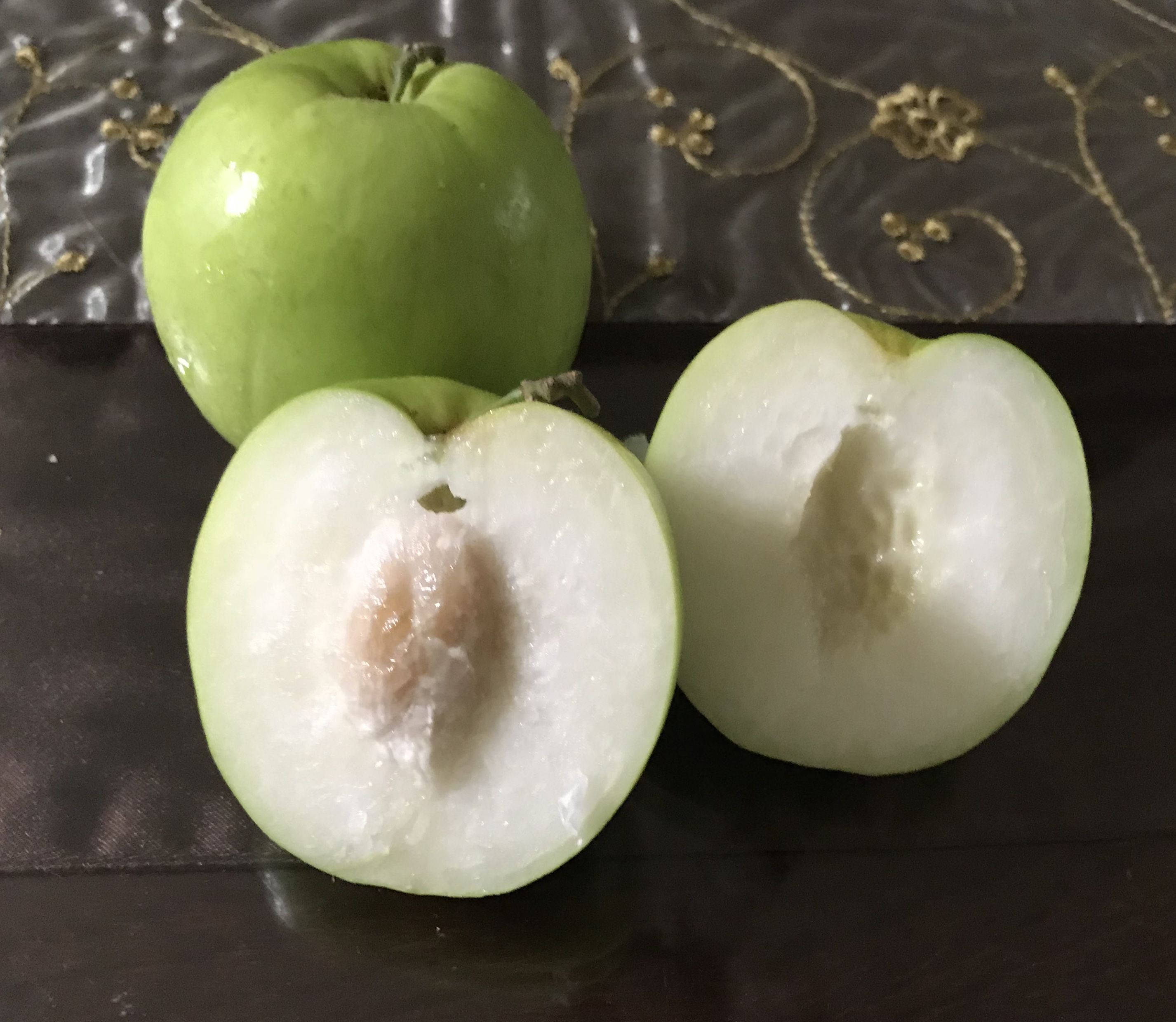 桂圓果切片 壁紙 — 一個完整和切半的綠色番石榴，帶有白色果肉和種子，放在深色圖案布料上。