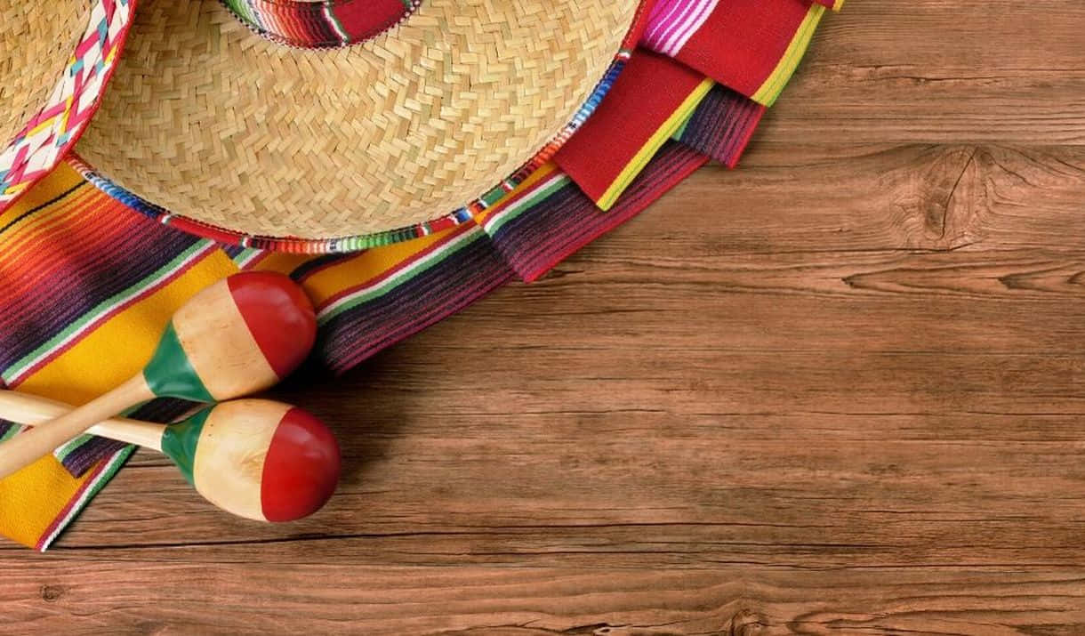 桌上墨西哥物品 Cinco de Mayo 背景 壁紙 — 一頂充滿活力的墨西哥闊邊帽、沙槌和色彩繽紛的塞拉佩放在質樸的木質表面上。