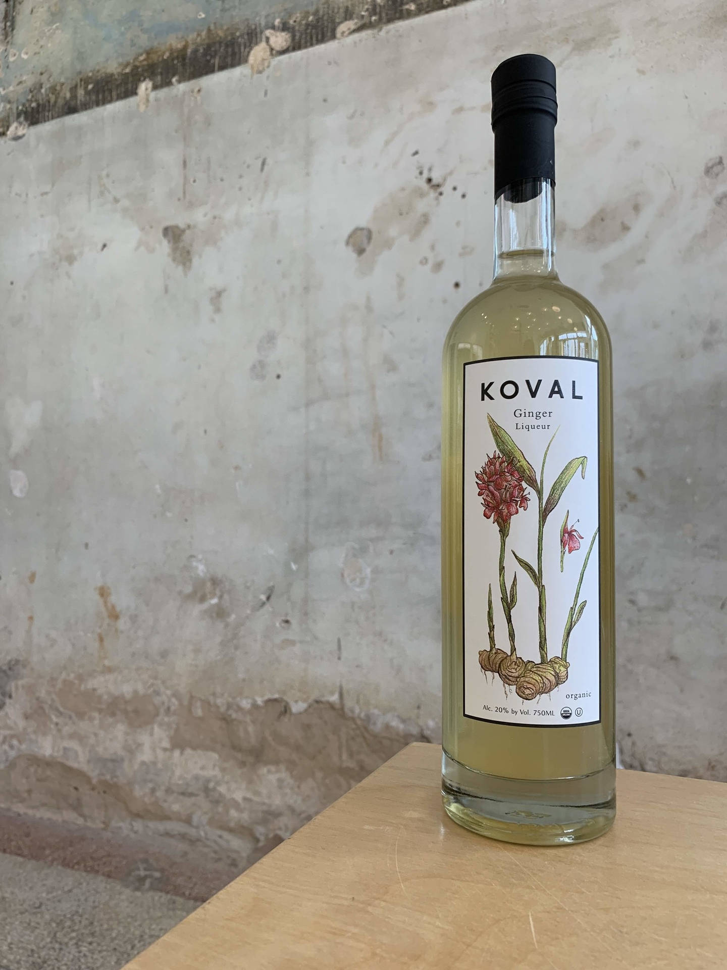 一瓶Koval Ginger Liqueur放在木頭上，背景是混凝土牆。