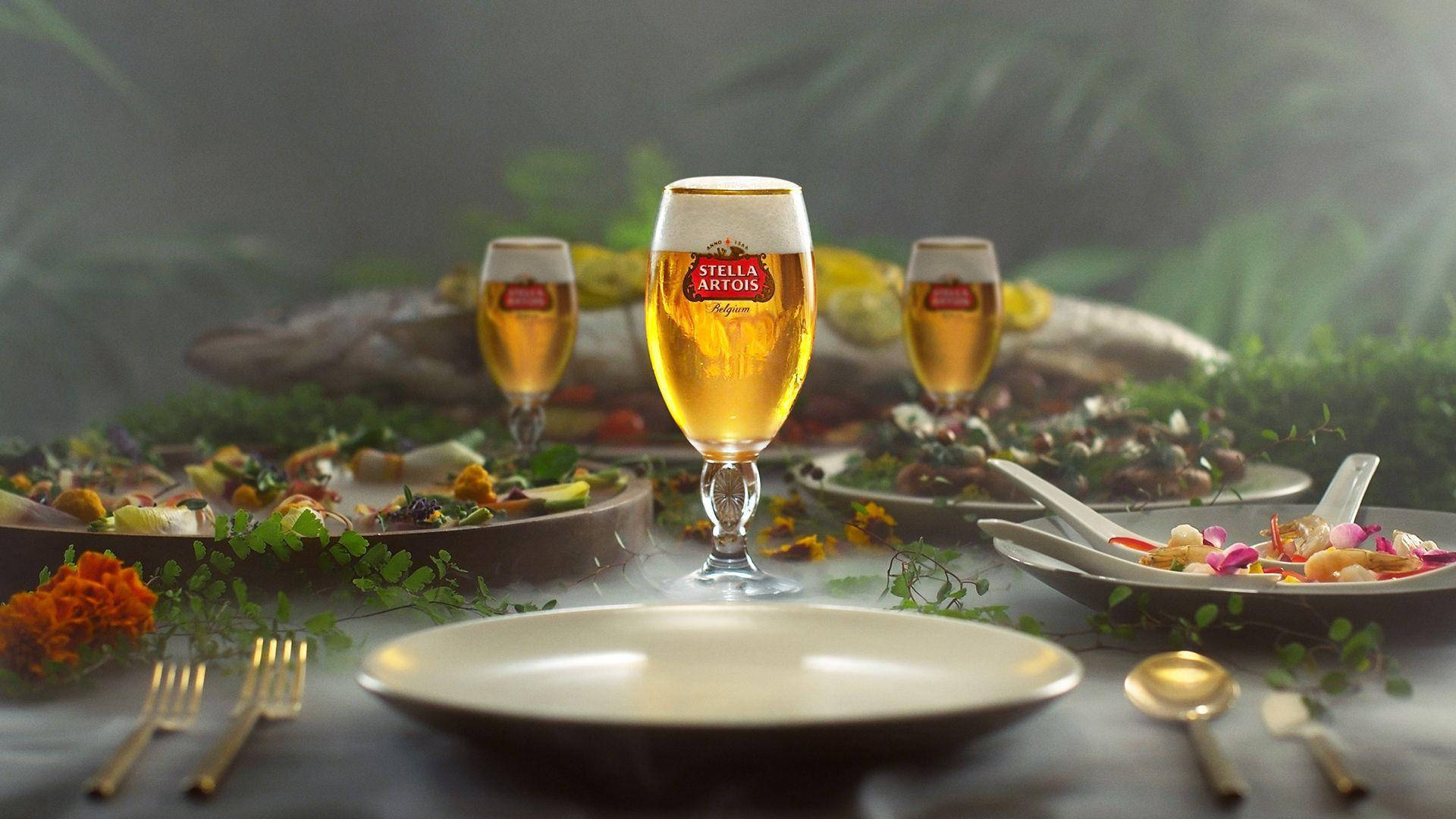 在霧氣瀰漫的花園環境中，擺放著 Stella Artois 啤酒和美食菜餚的桌子。