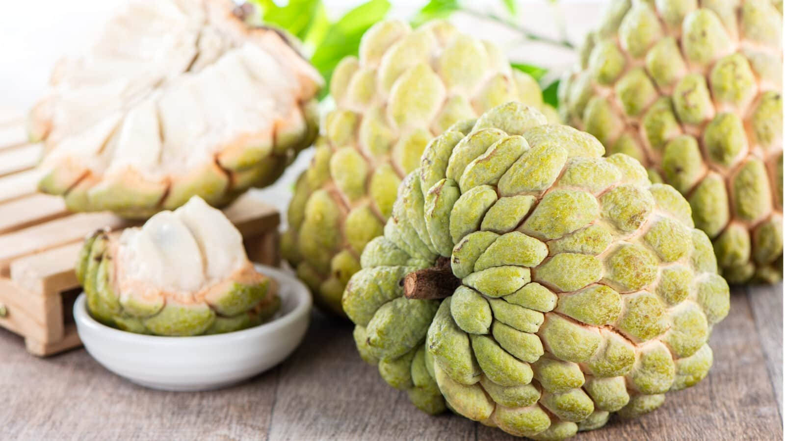 桌上的糖蘋果 壁紙 — 新鮮綠色牛油果（釋迦）帶有紋理外皮和奶油白色果肉，展示在質樸木質表面上。