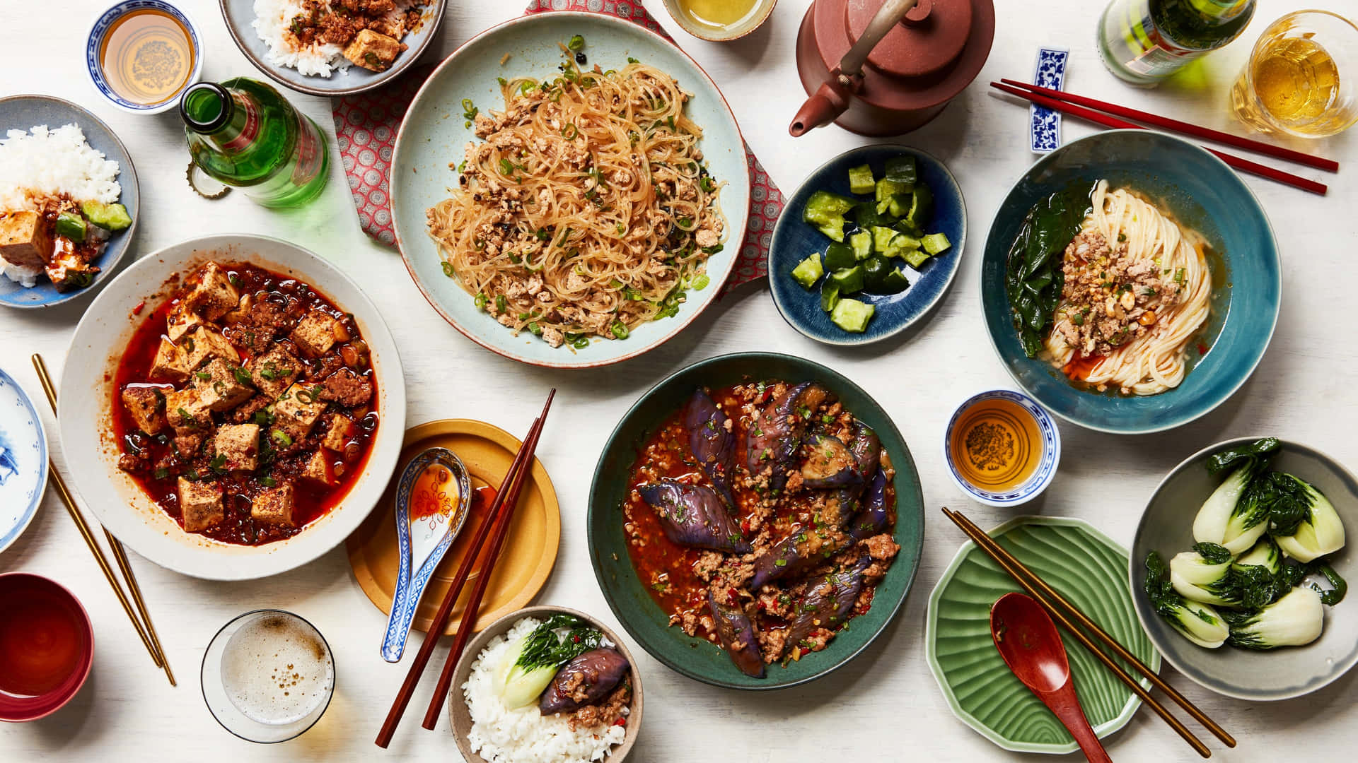 色彩繽紛的亞洲菜餚，包括麵條、豆腐和茄子，盛在陶瓷碗中，附有筷子和飲料。
