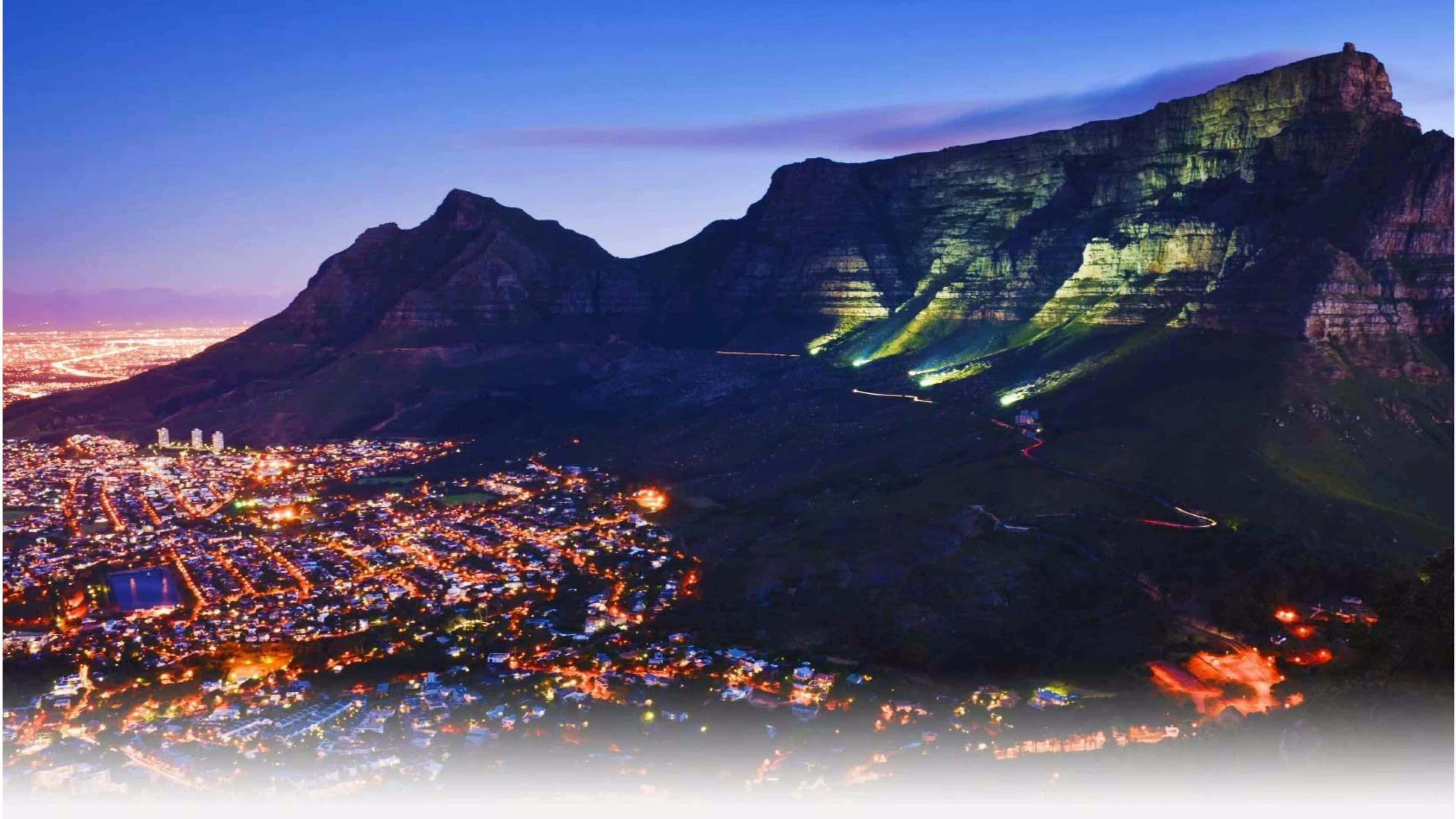 South Africa 桌布 壁紙 — 桌山在暮色中的鳥瞰圖，城市燈光在下方閃爍，照明小徑蜿蜒而上。