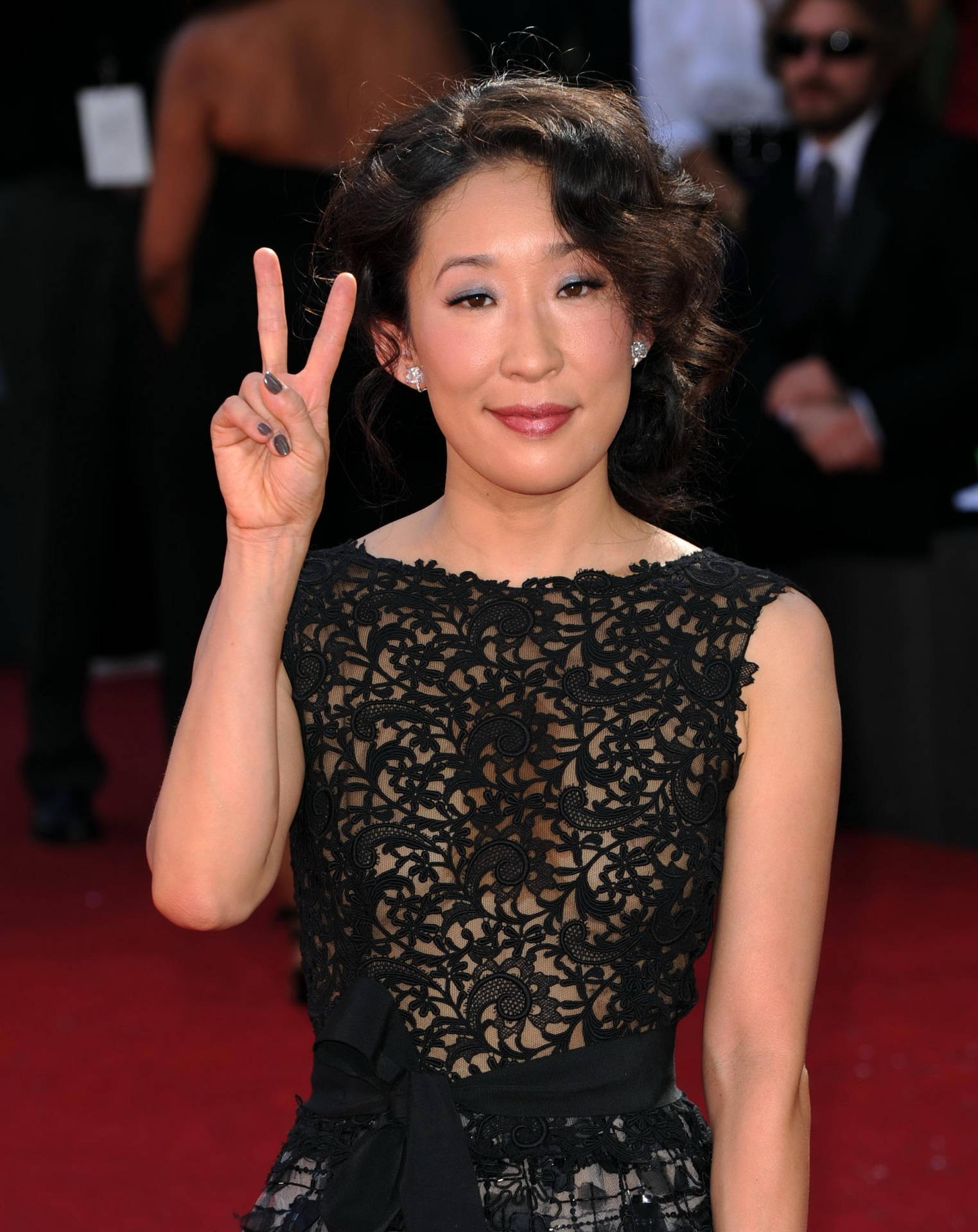 身穿黑色蕾絲裙的女性在紅地毯上比出和平手勢