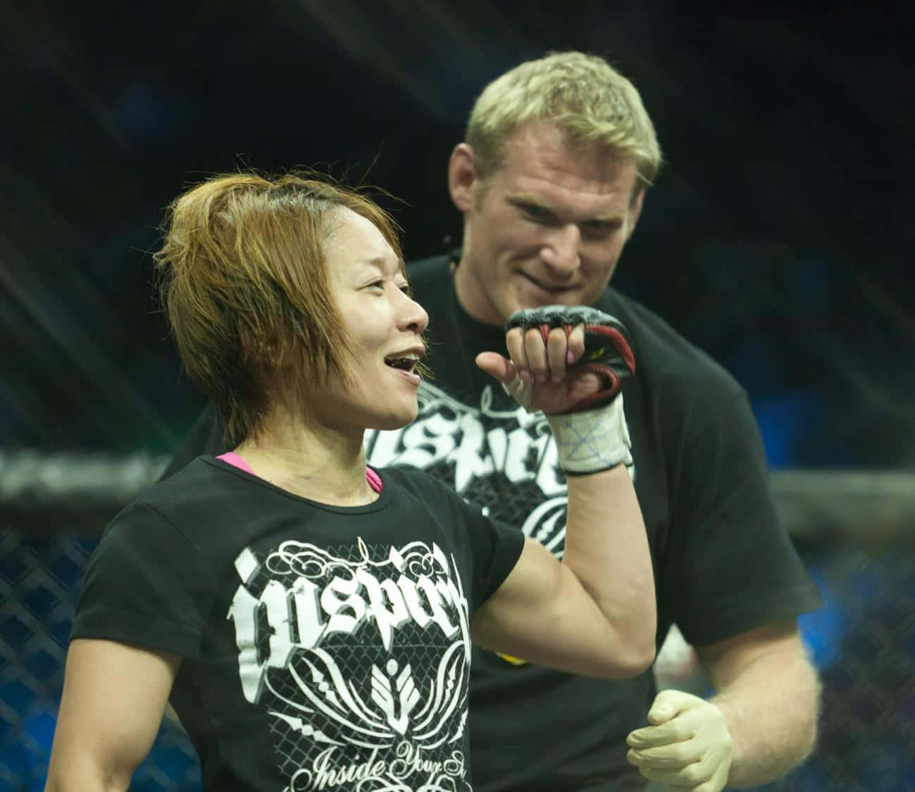 梅古美·藤井與教練喬什·巴內特 壁紙 — 一名女拳手在籠中慶祝勝利，身後有一位微笑的教練。