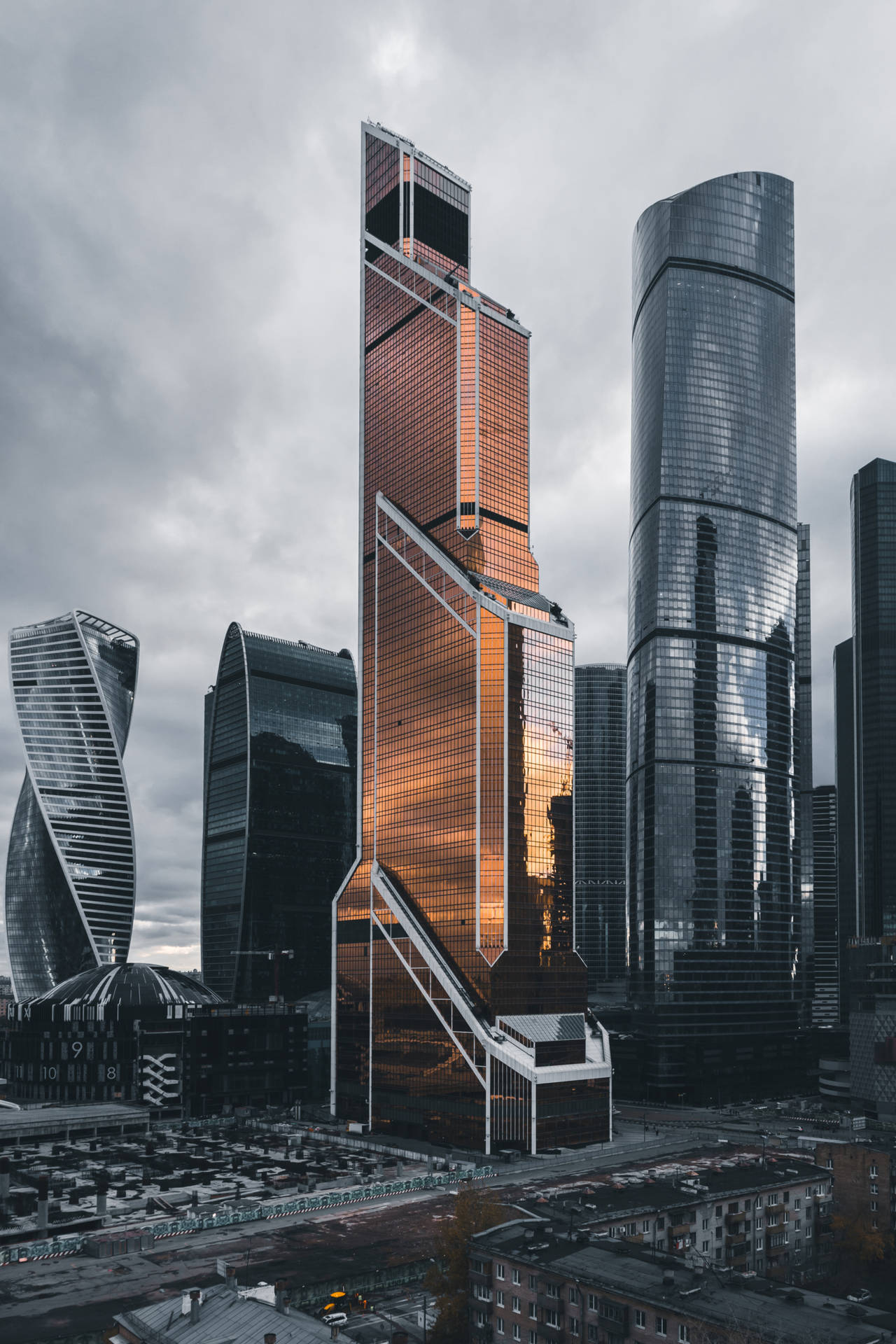 高聳的玻璃摩天大樓在多雲的城市景觀中反射夕陽光線。