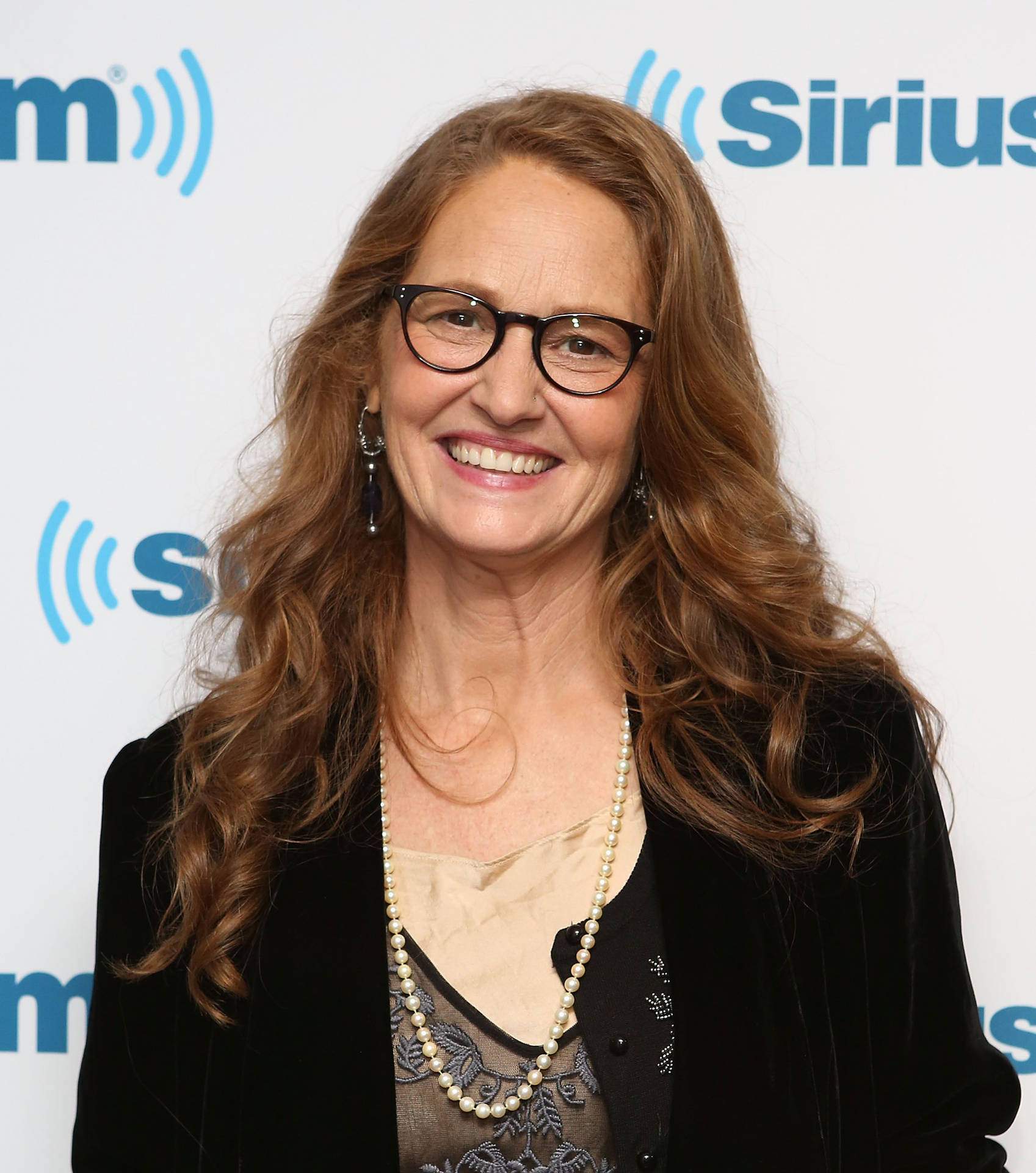 戴眼鏡和珍珠項鍊的女士在SiriusXM活動中對著鏡頭微笑。