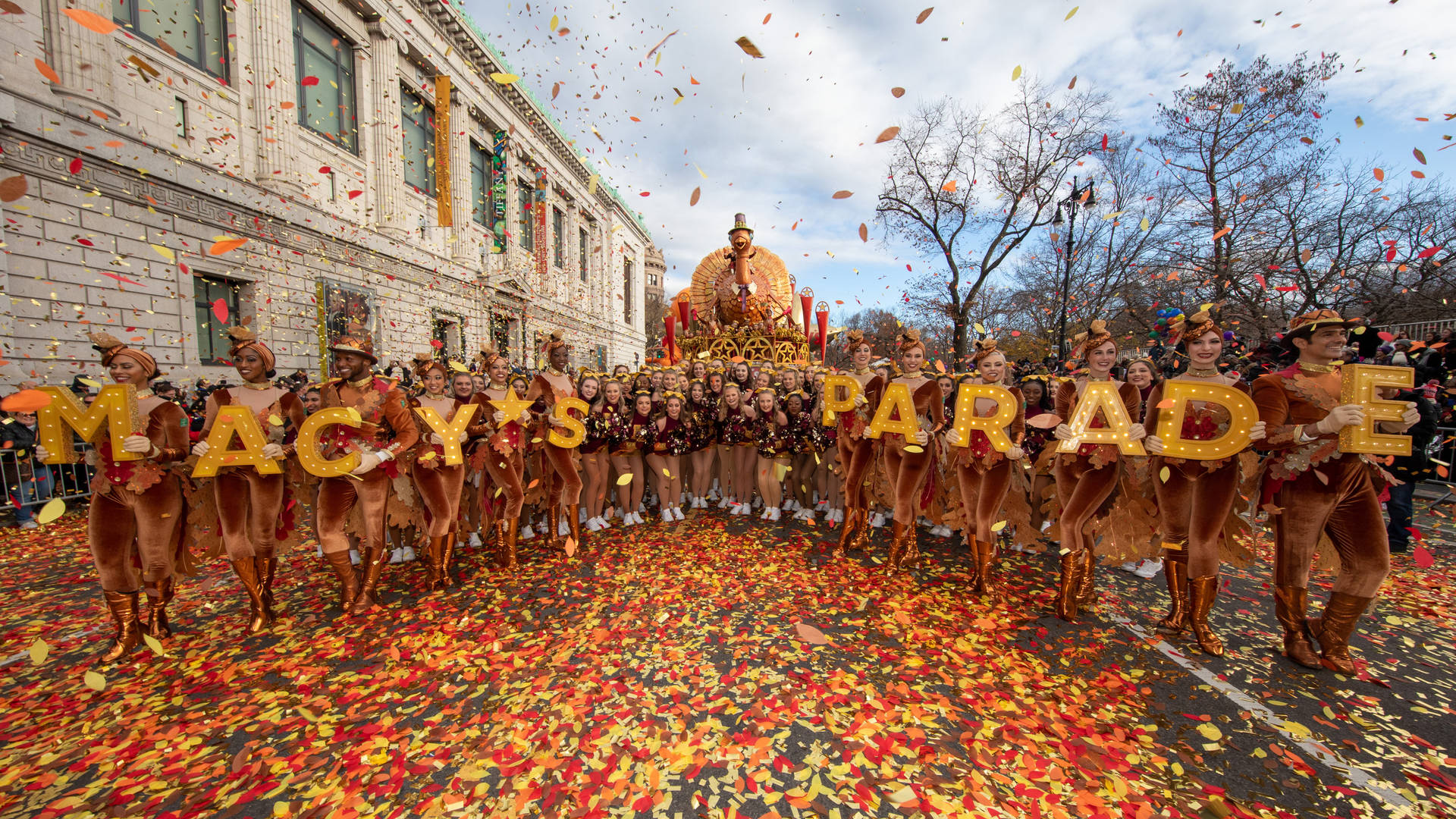 Macy's Parade 表演者身穿秋季服裝，在街道上飄落的五彩紙屑中。