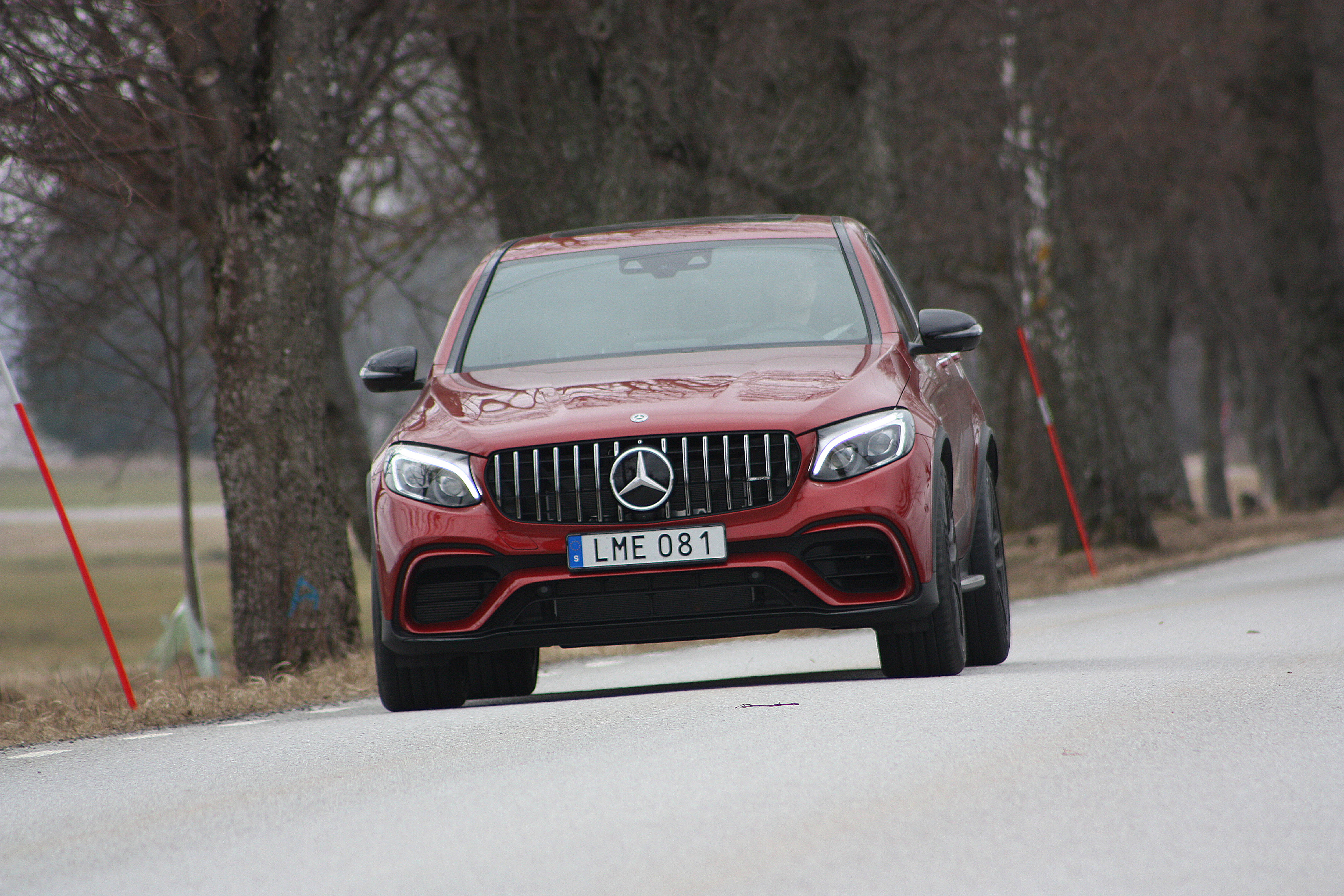 梅賽德斯-AMG GLC Coupe 壁紙 — 一輛亮紅色的Mercedes-AMG GLE63 S SUV在陰天自信地行駛在綠樹成蔭的道路上。